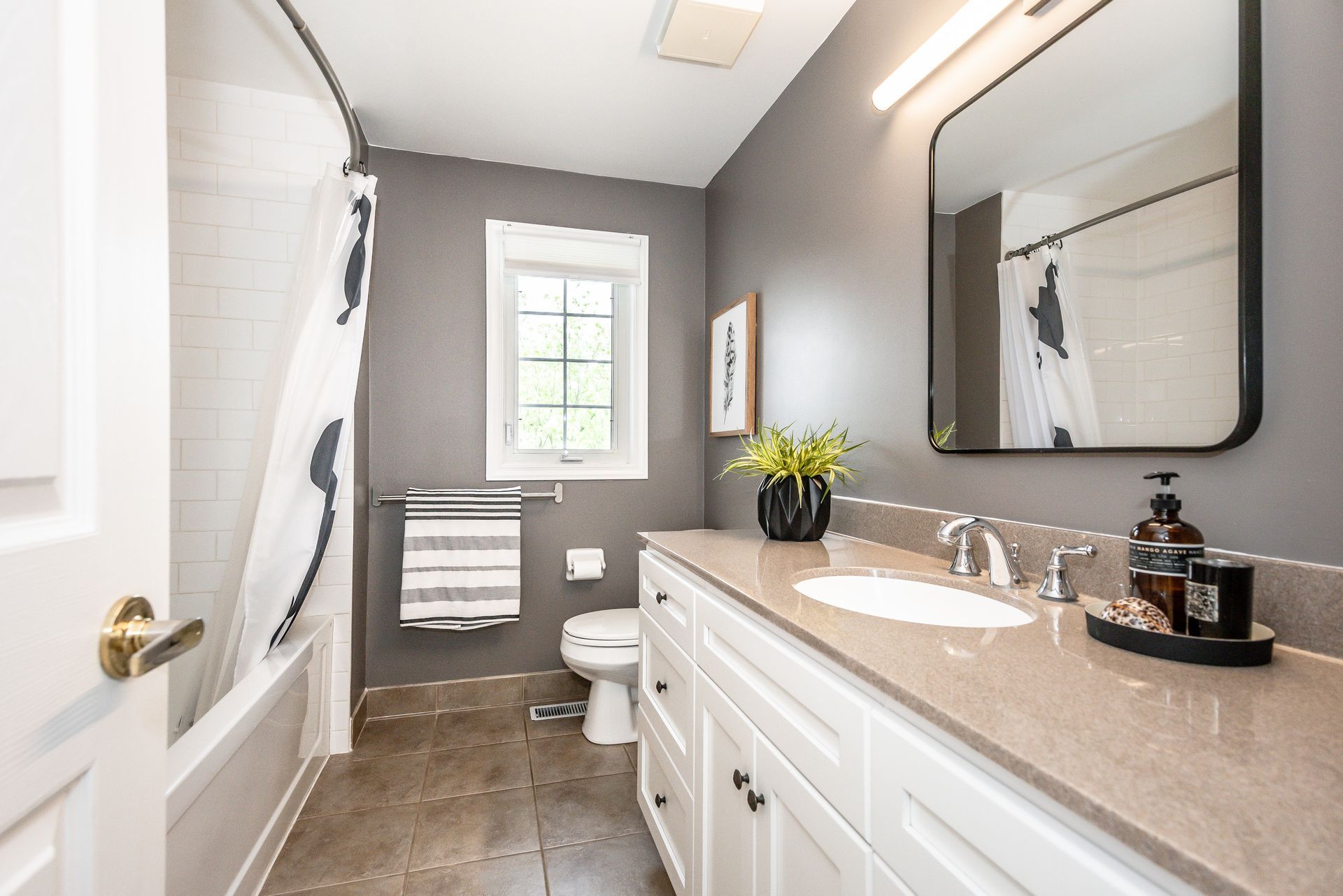 Bright modern bathroom with white vanity, gray walls, window, shower curtain, and dark tile floor