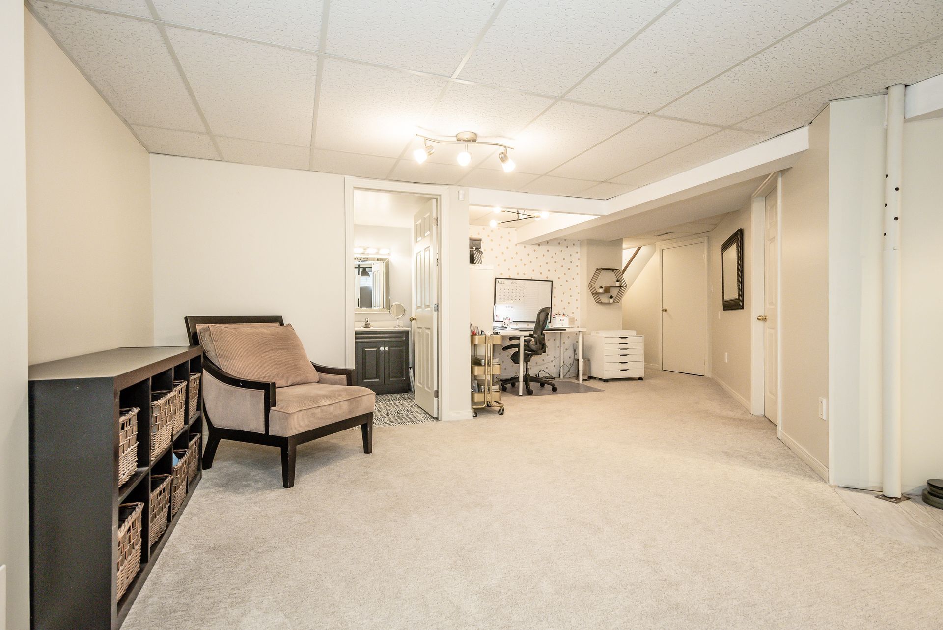 Spacious beige basement living room with a chaise, shelving, and a desk area near a doorway