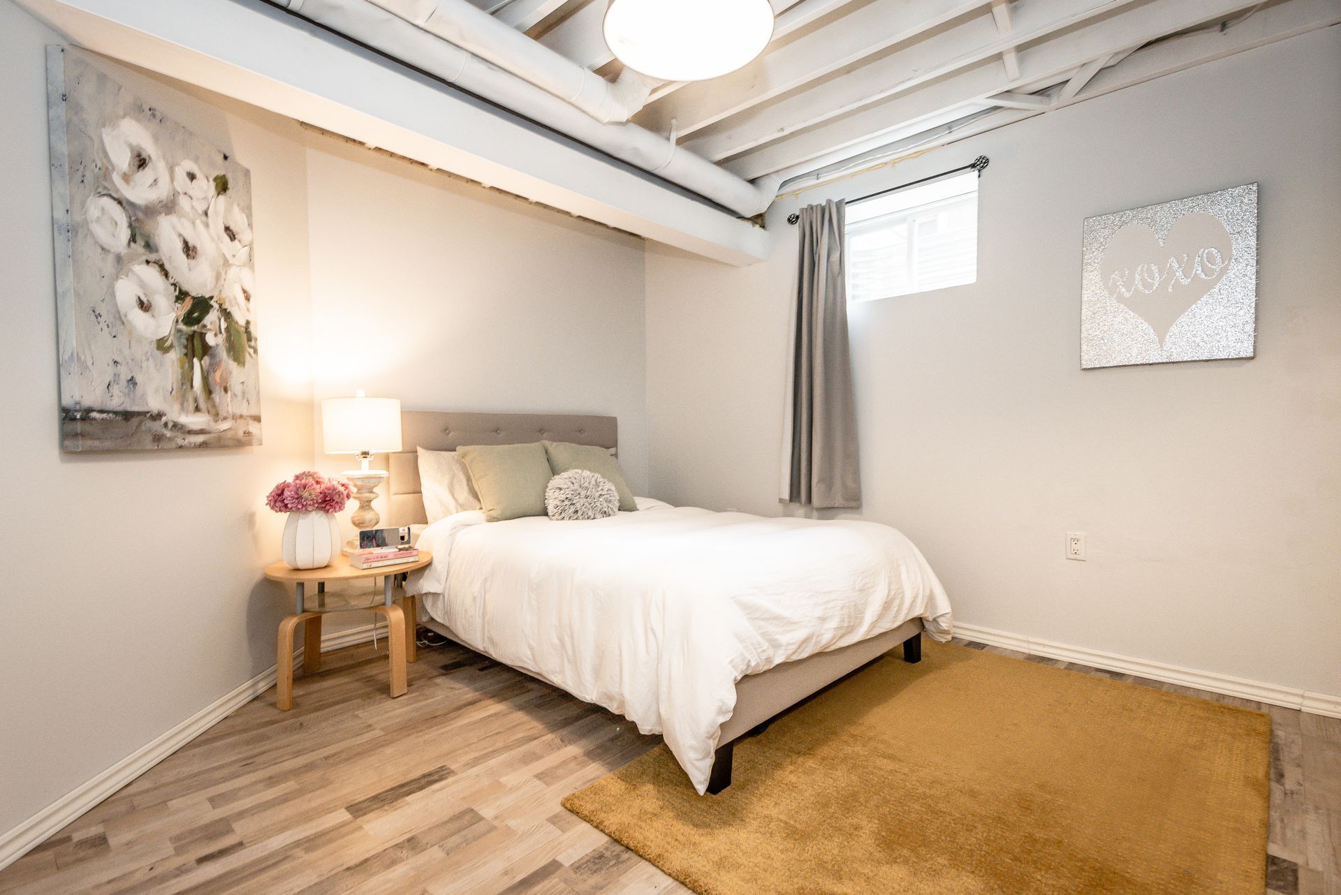 Minimal bedroom with a white bed, wooden nightstand, tan rug, and wall art in a bright modern room