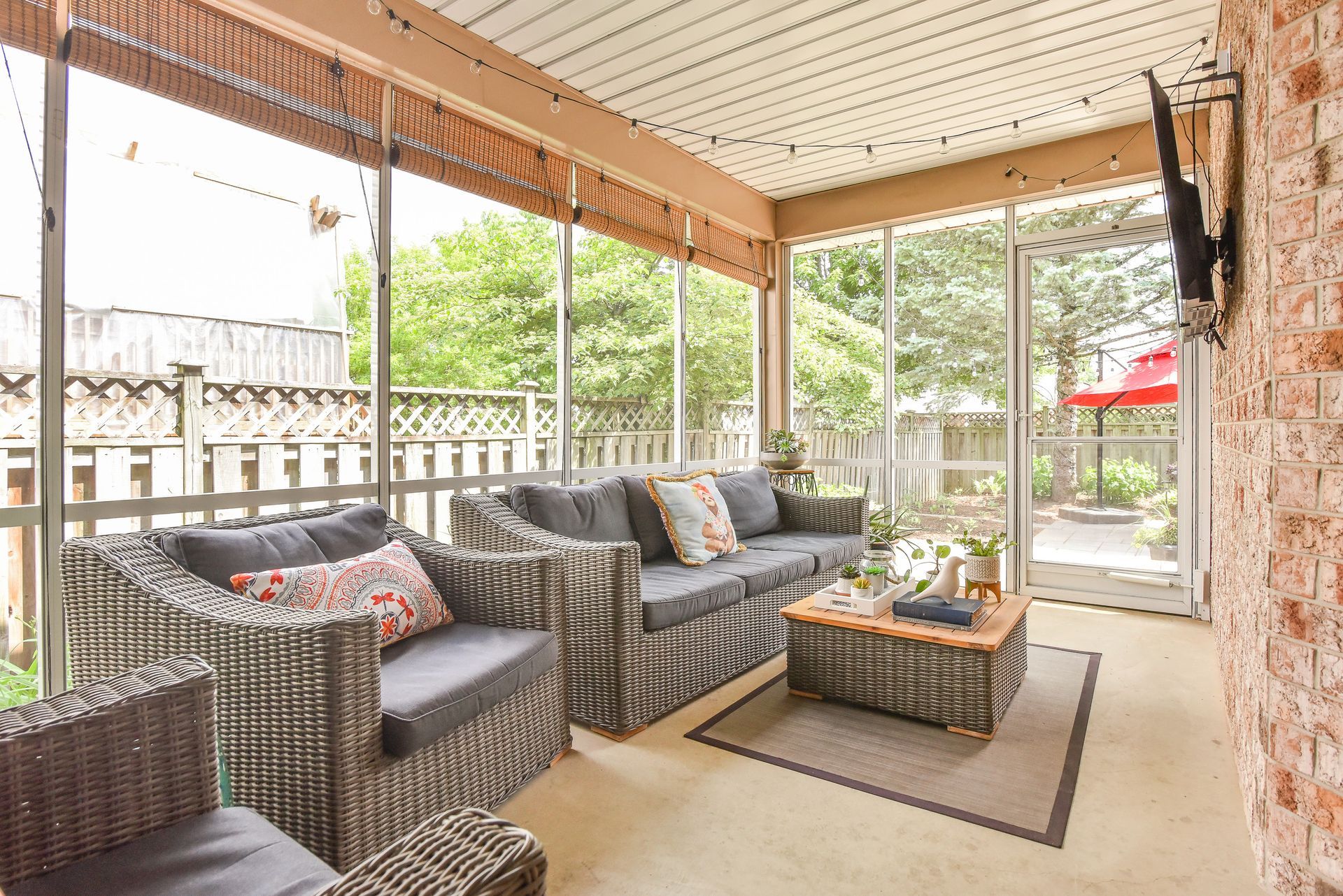Covered patio with wicker sectional, coffee table, and sliding glass doors overlooking a garden