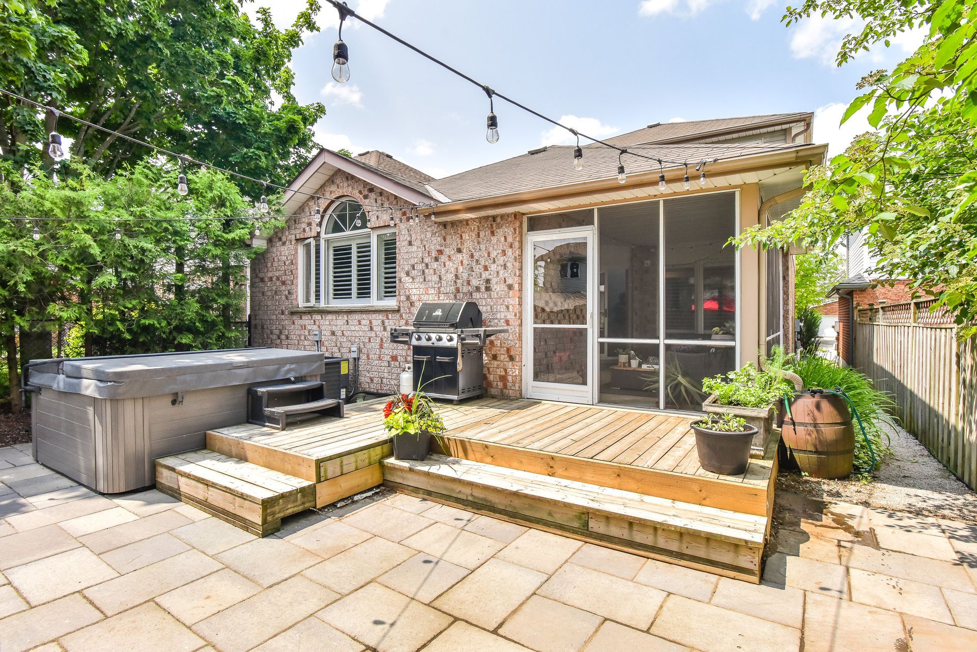 Brick patio with hot tub, grill, and sliding glass door in a sunny backyard
