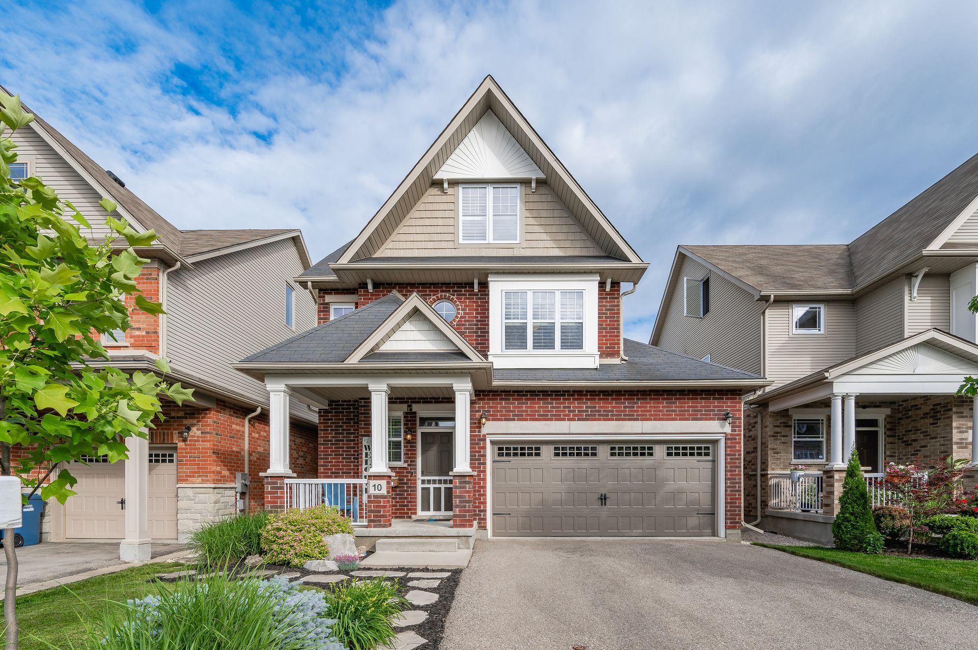 Suburban two-story brick house with a front porch, garage, and driveway under a blue sky