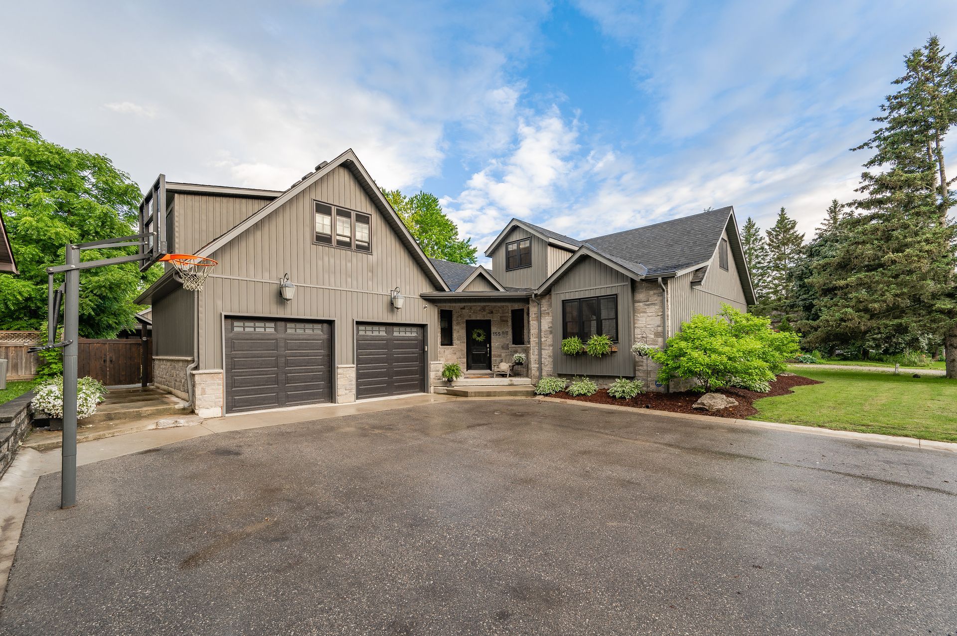 Suburban house with two-car garage, stone entryway, and landscaped front yard under a cloudy sky