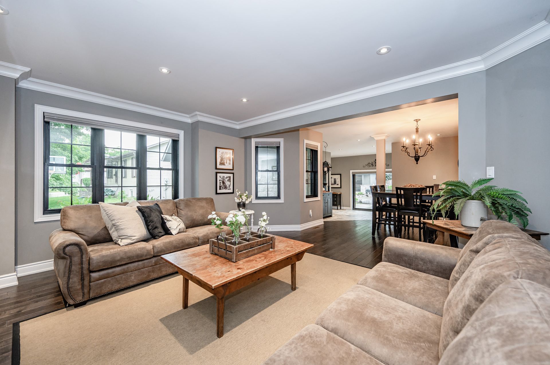 Bright living room with beige sofas, wooden coffee table, large window, and dining area beyond the archway