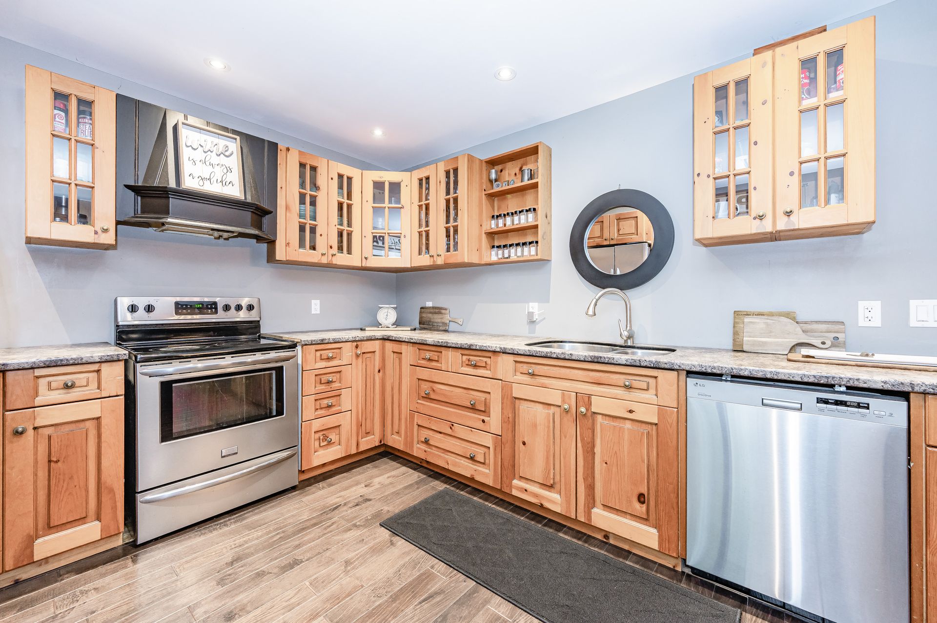 Bright modern kitchen with light wood cabinets, stainless steel appliances, granite counters, and a round wall clock