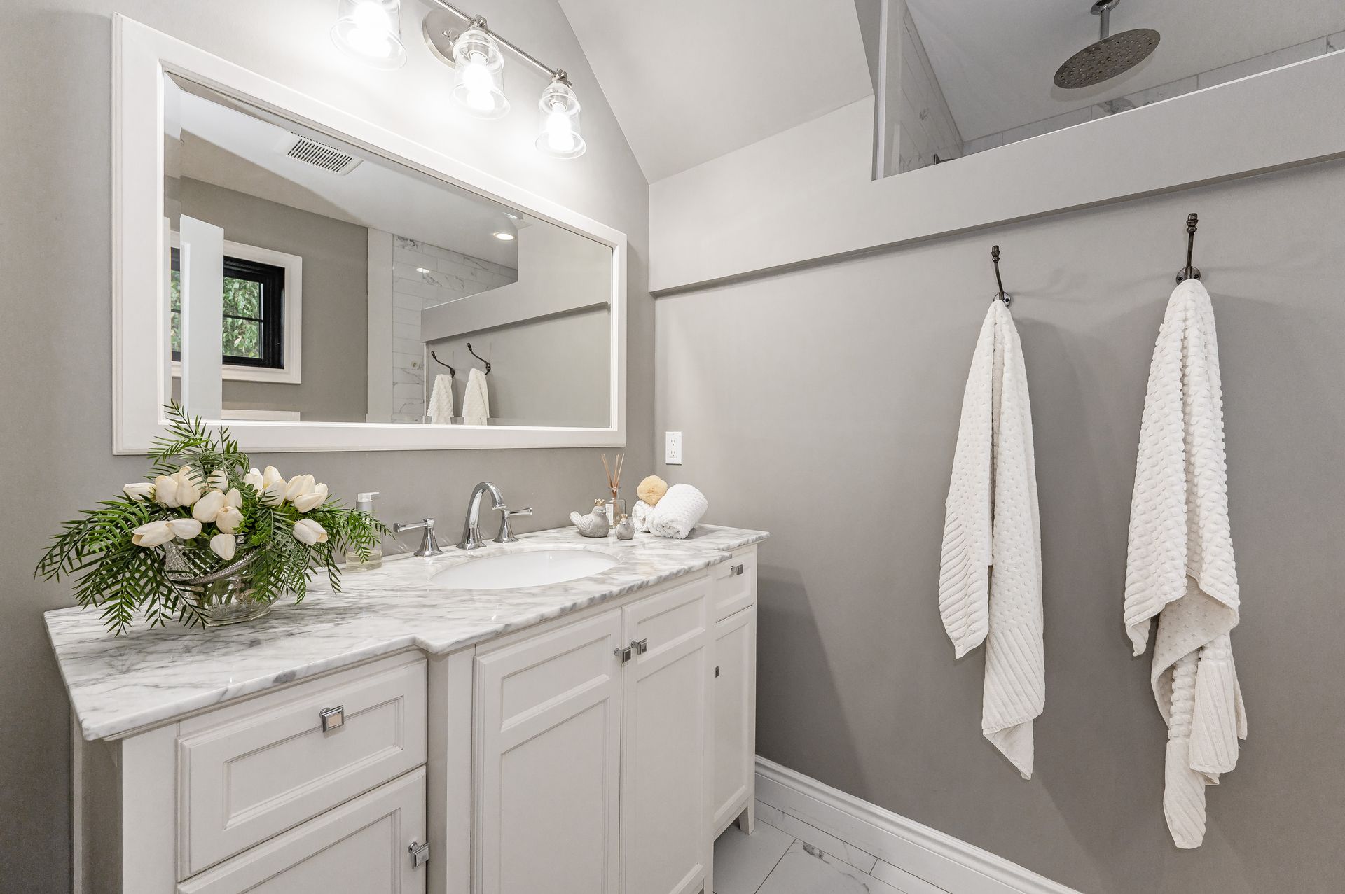 Bright white bathroom with vanity, mirror, sink, towels, and a shower area.