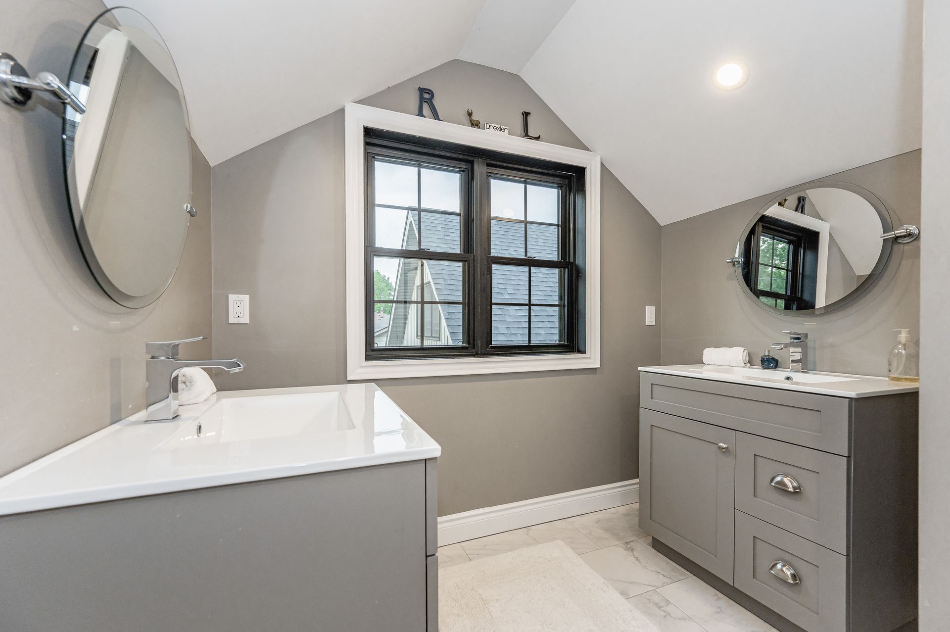 Bright bathroom with double vanity, wall mirrors, and a window under a sloped ceiling.