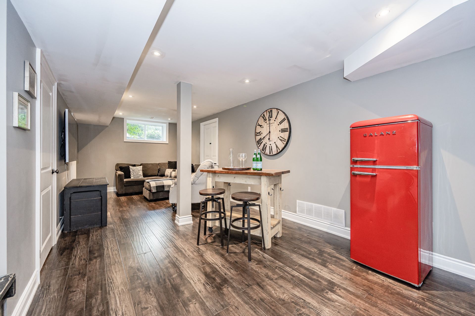 Modern open kitchen and living area with red fridge, wood floors, and a dining table next to a large wall clock