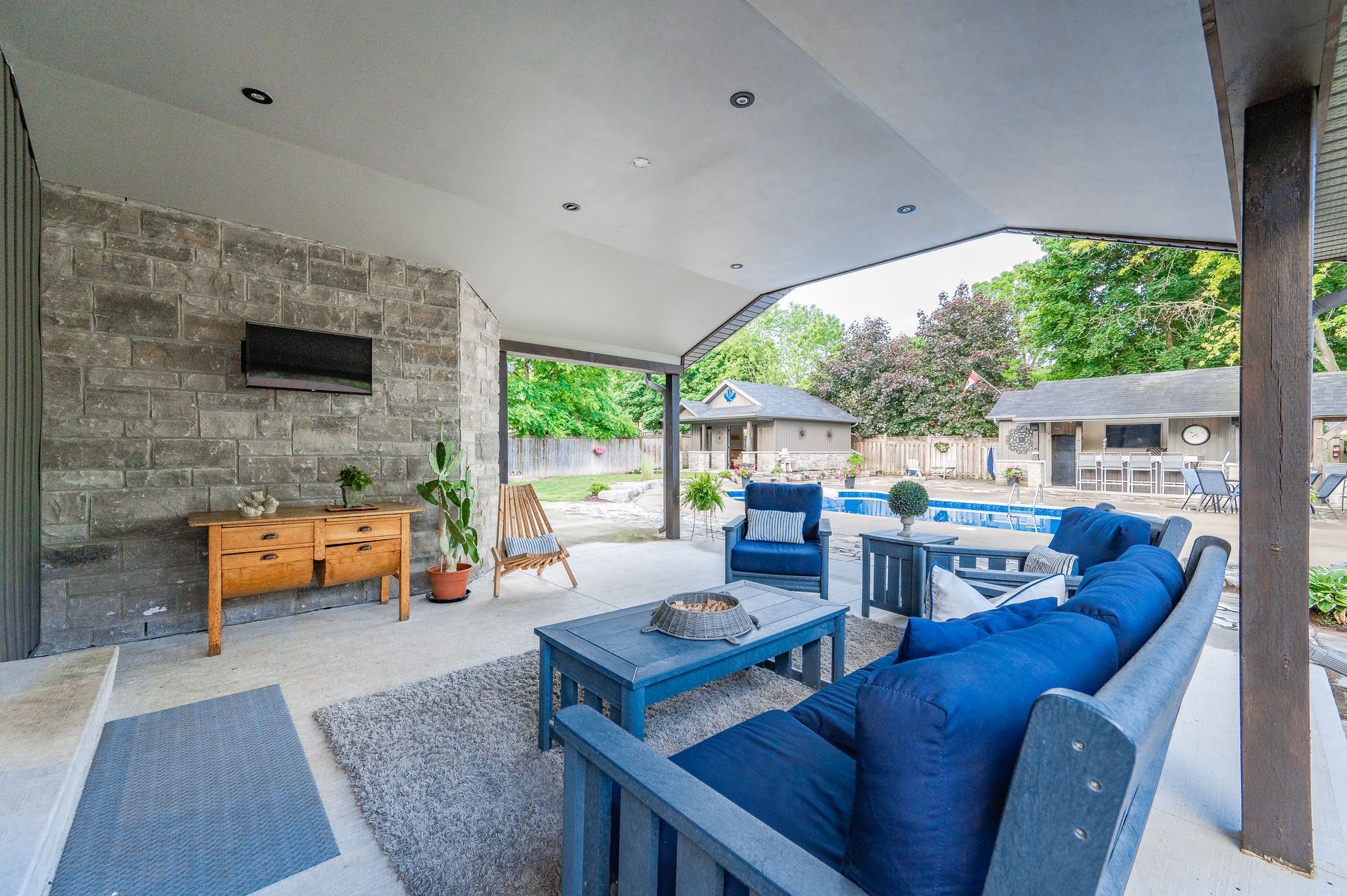 Covered outdoor patio with blue sectional seating, stone fireplace, and dining area
