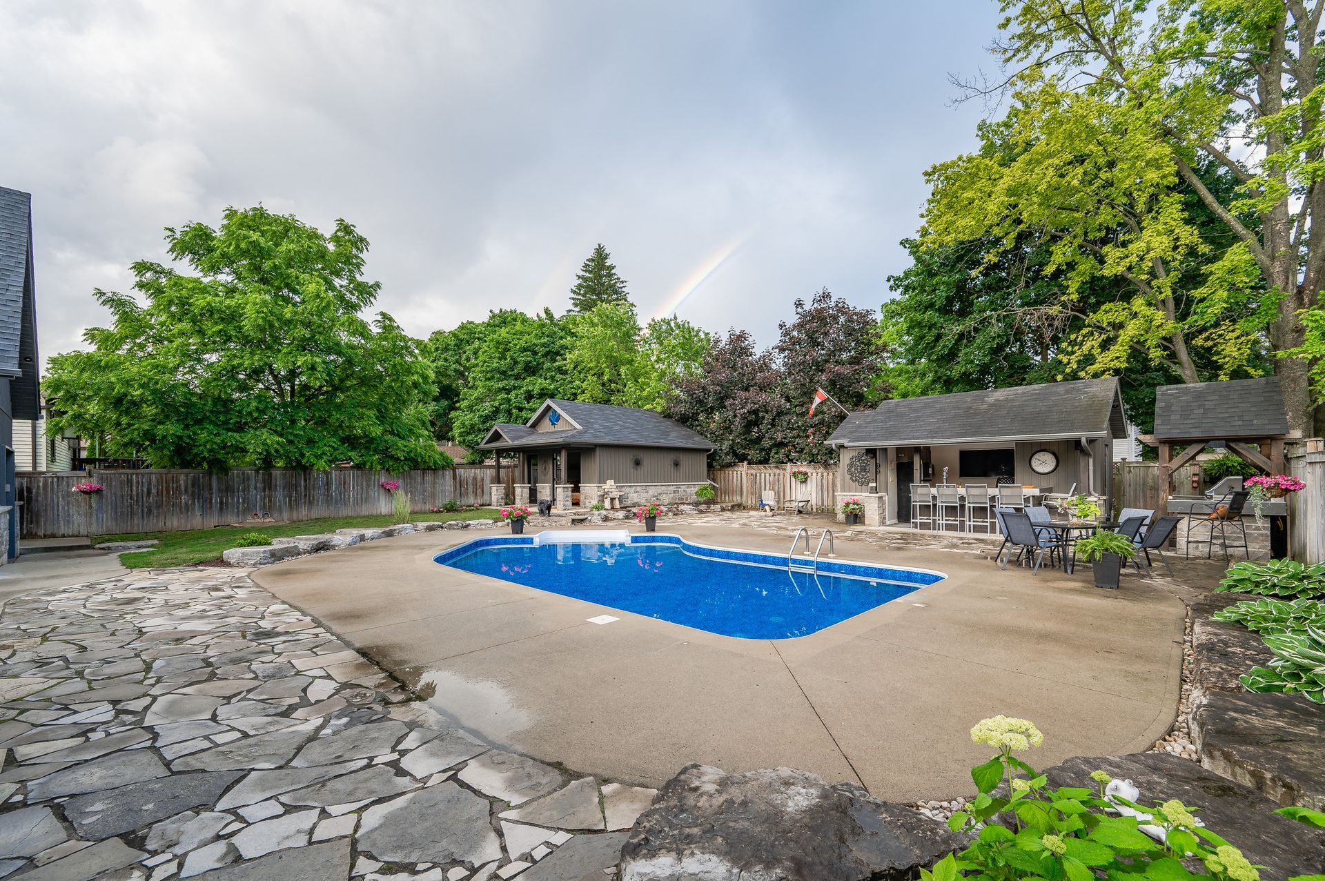 Backyard pool with blue cover, stone patio, and surrounding trees and lounge area
