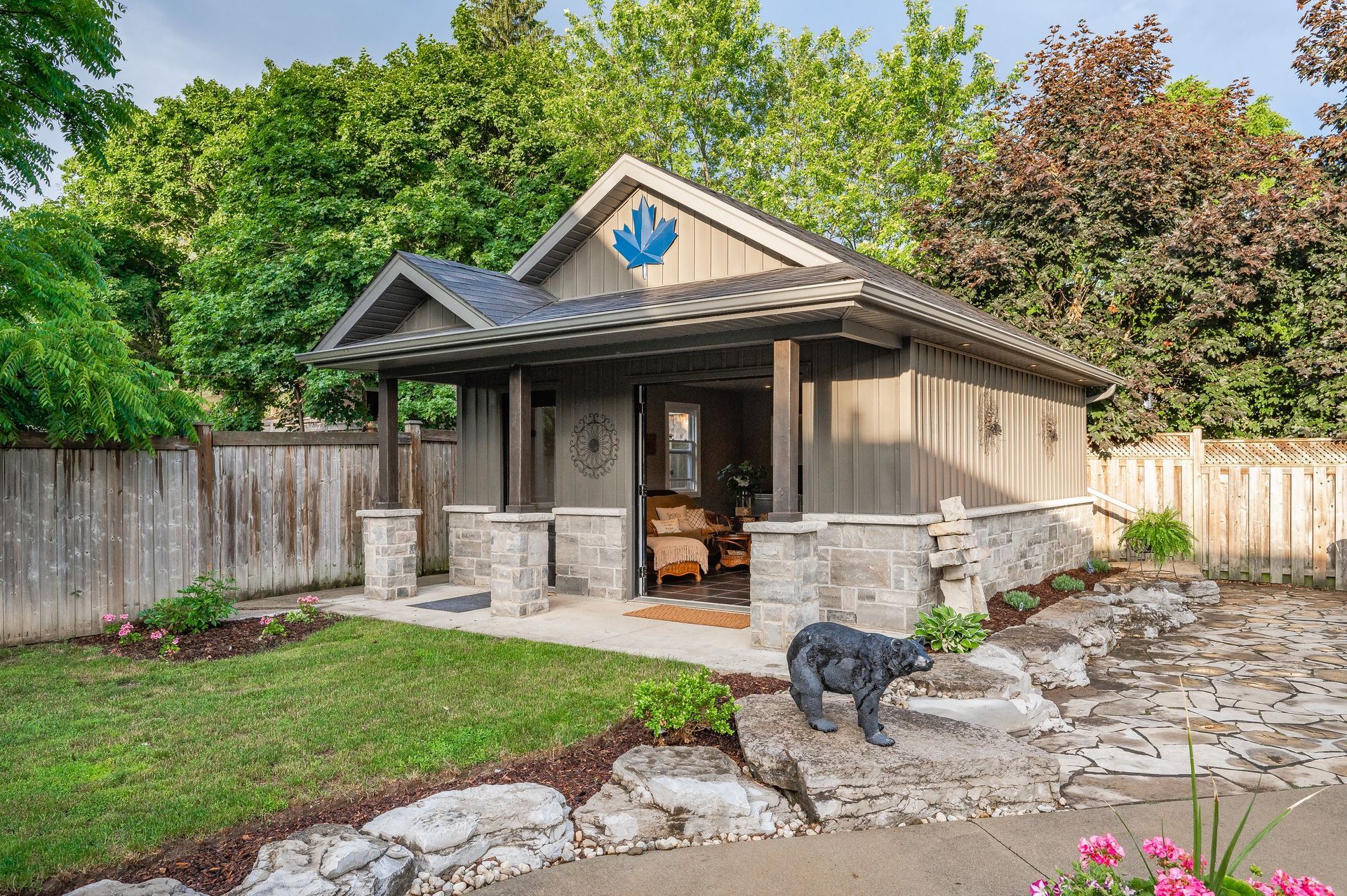 Stone backyard gazebo with porch, surrounded by trees and a small black dog in front