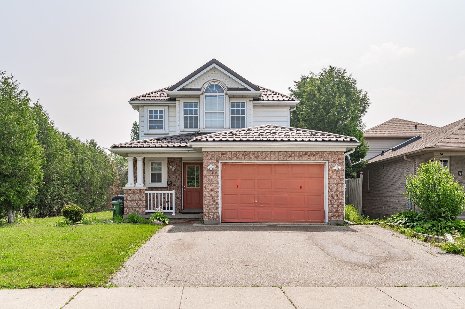 Two-story suburban house with a red garage door, front lawn, and driveway