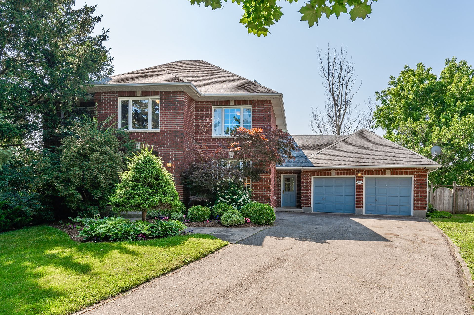 Two-story brick house with double garage, curved driveway, and green front yard on a sunny day