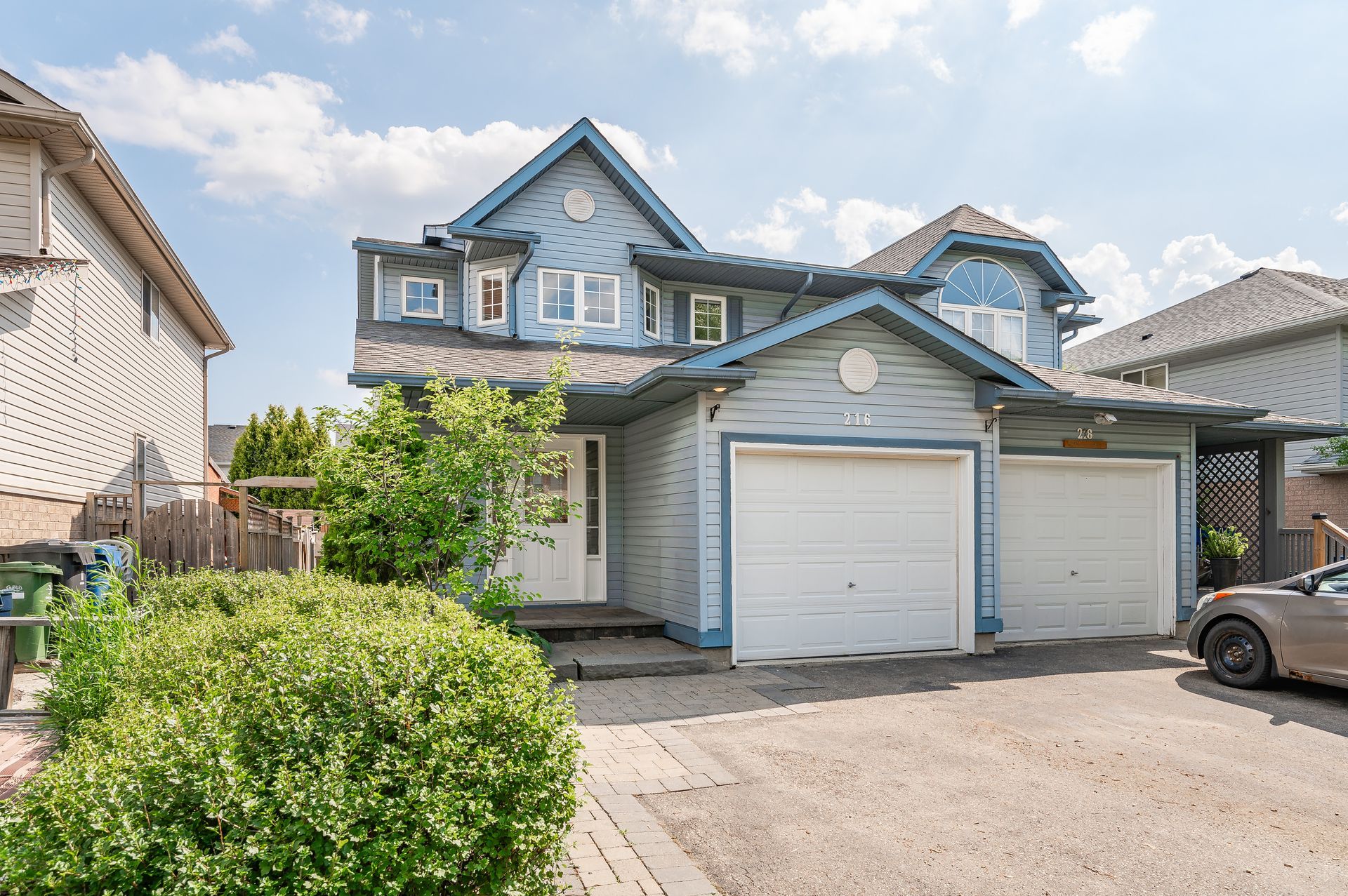 Blue two-story house with double garage and driveway under a partly cloudy sky