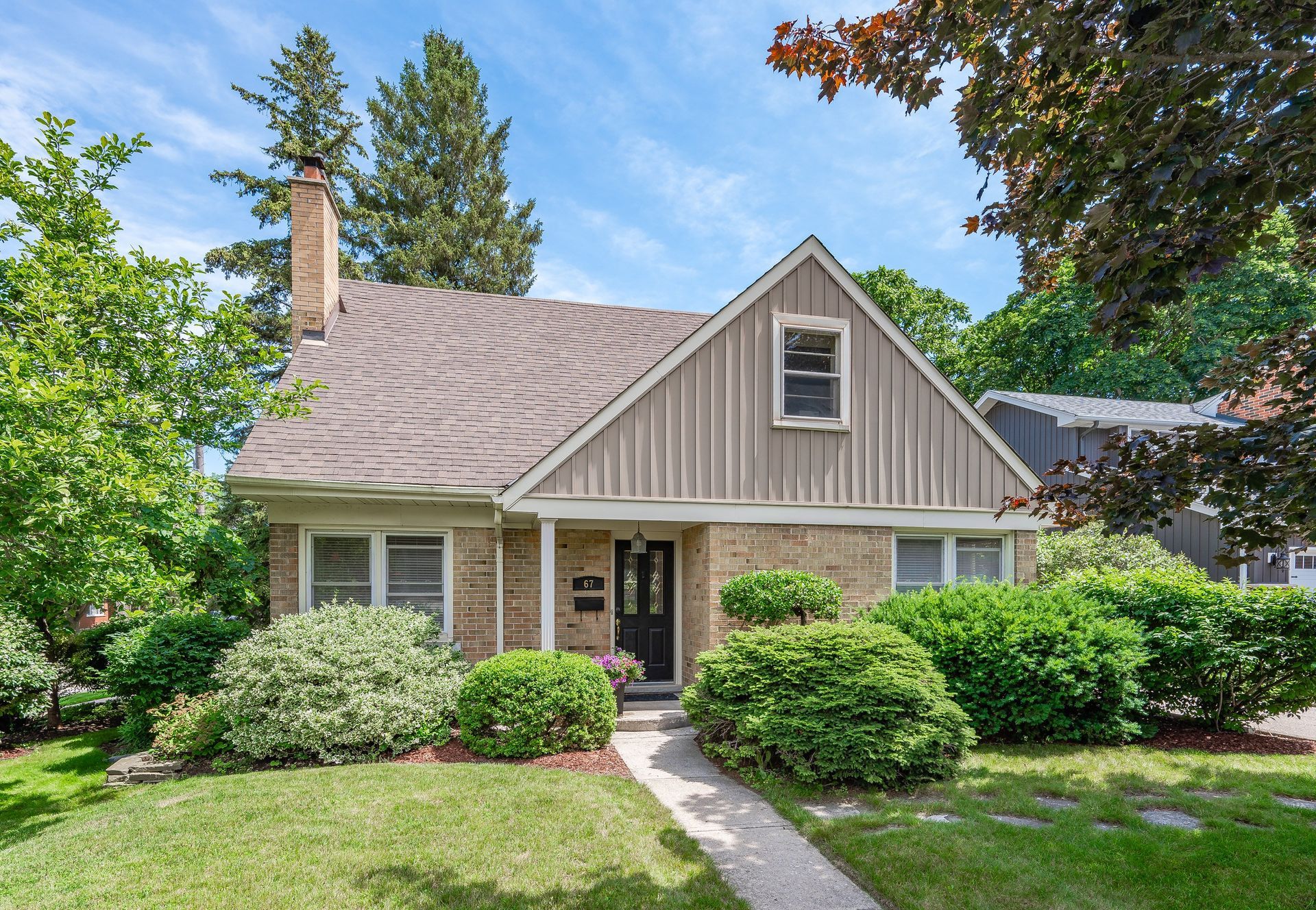 Suburban house with beige siding, front porch, and manicured shrubs along a stone walkway
