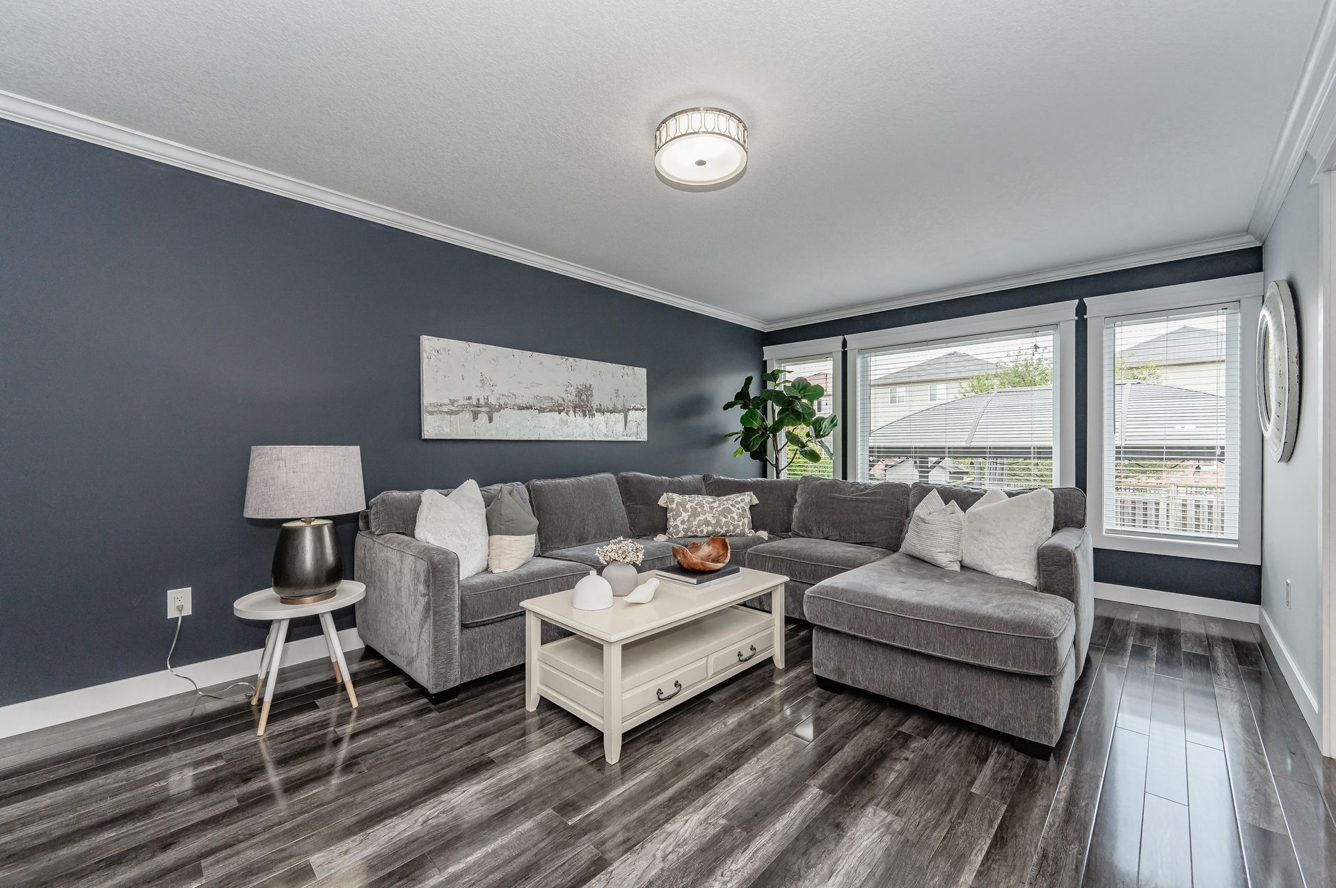 Gray living room with sectional sofa, coffee table, lamp, and large windows overlooking greenery