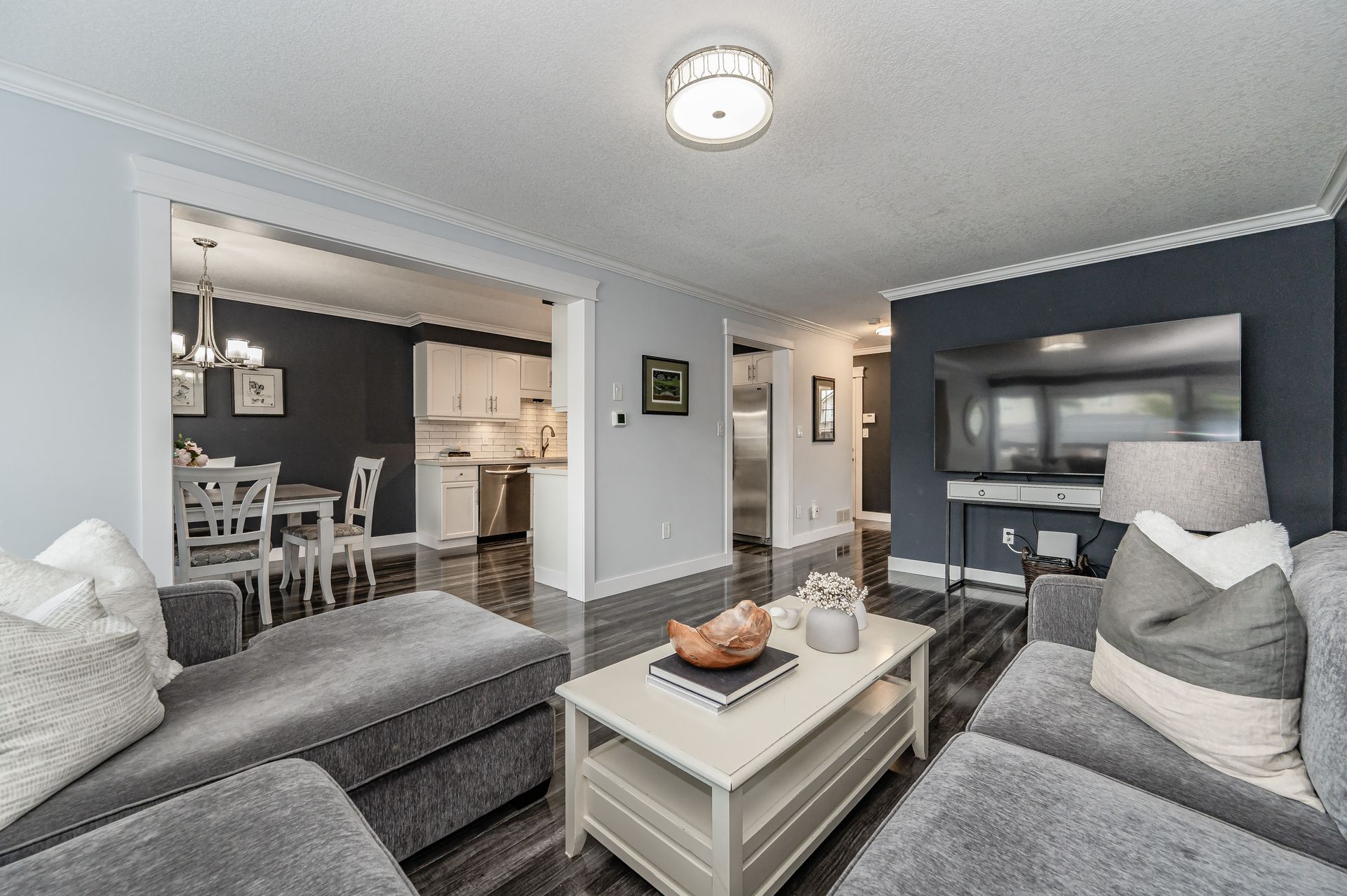 Gray living room with sectional sofas, coffee table, and open view into a dining area and kitchen.
