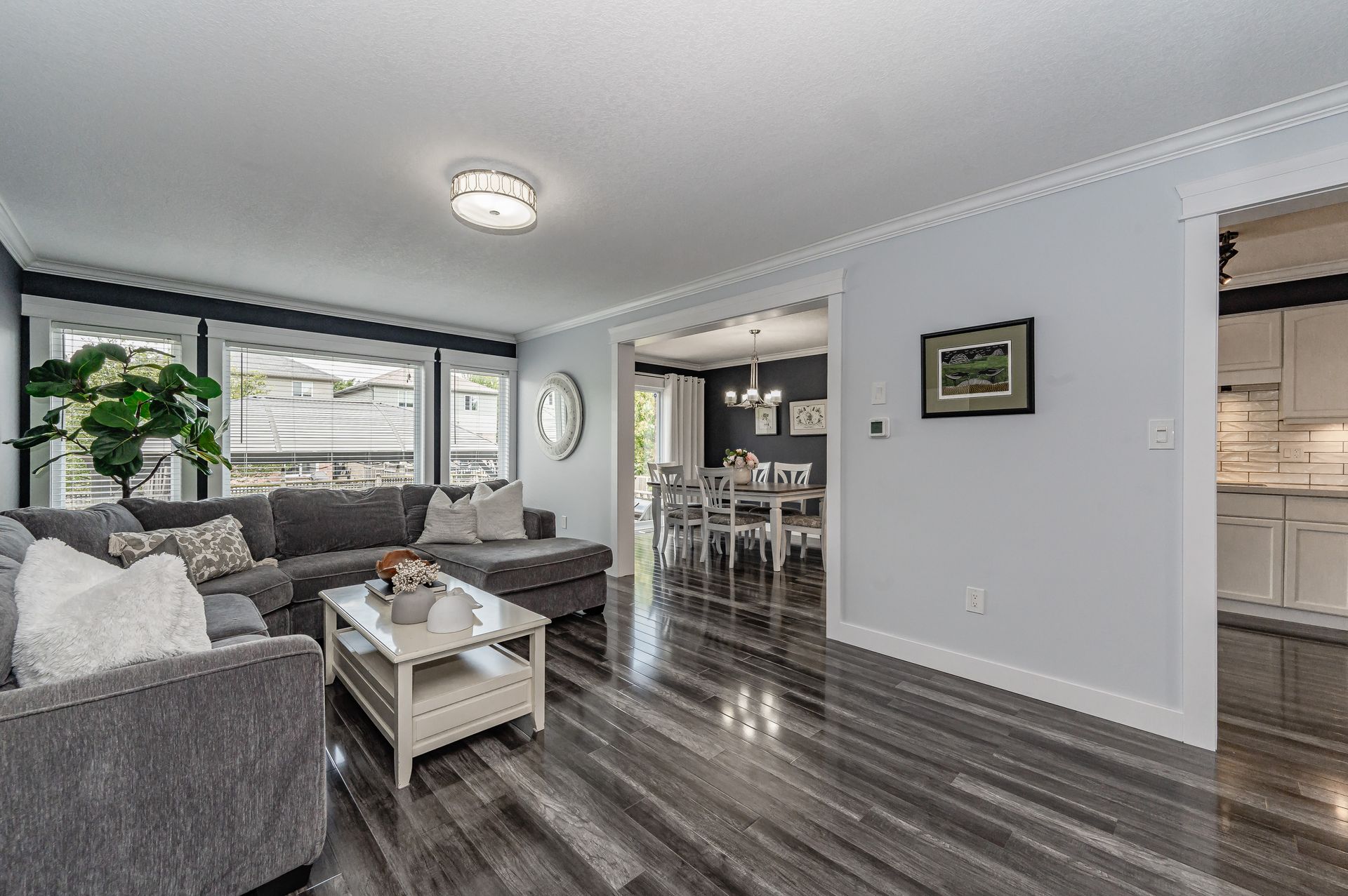 Bright living room with gray sectional, coffee table, wall art, and open view to dining and kitchen areas.