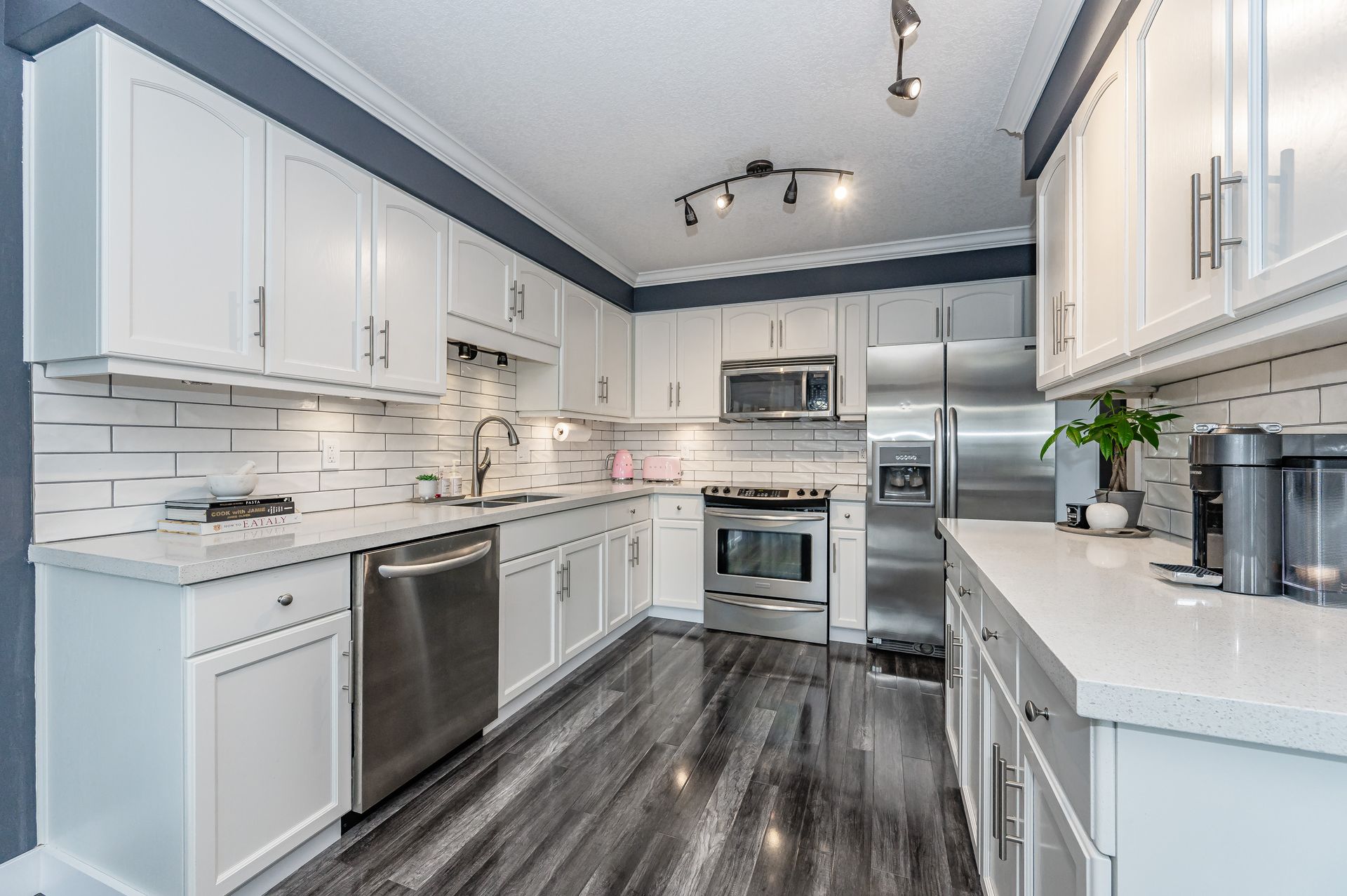 Modern white kitchen with stainless steel appliances, dark flooring, and bright recessed lighting