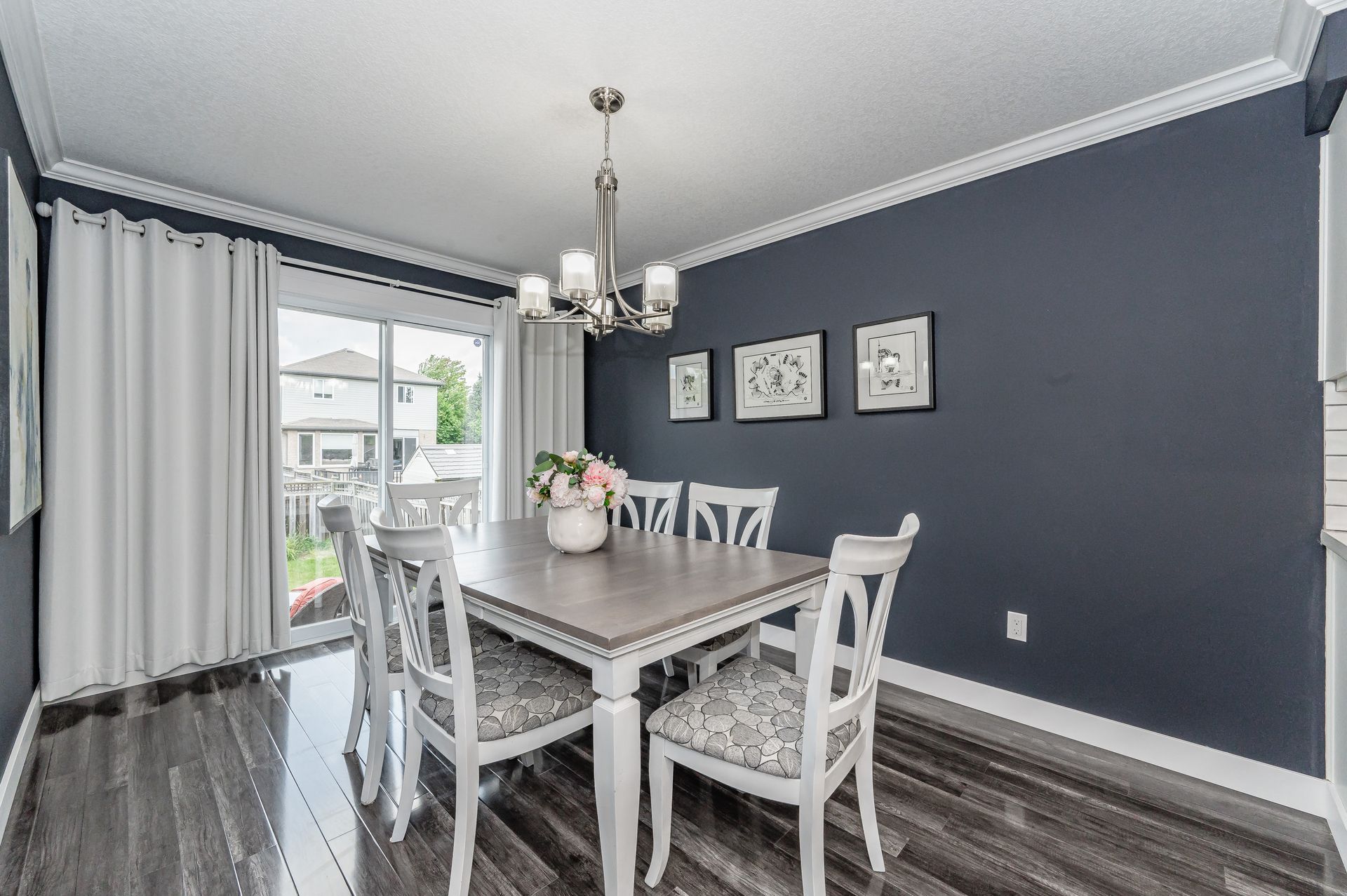 Modern dining room with white table and chairs, gray walls, dark wood floor, and sliding glass door to patio