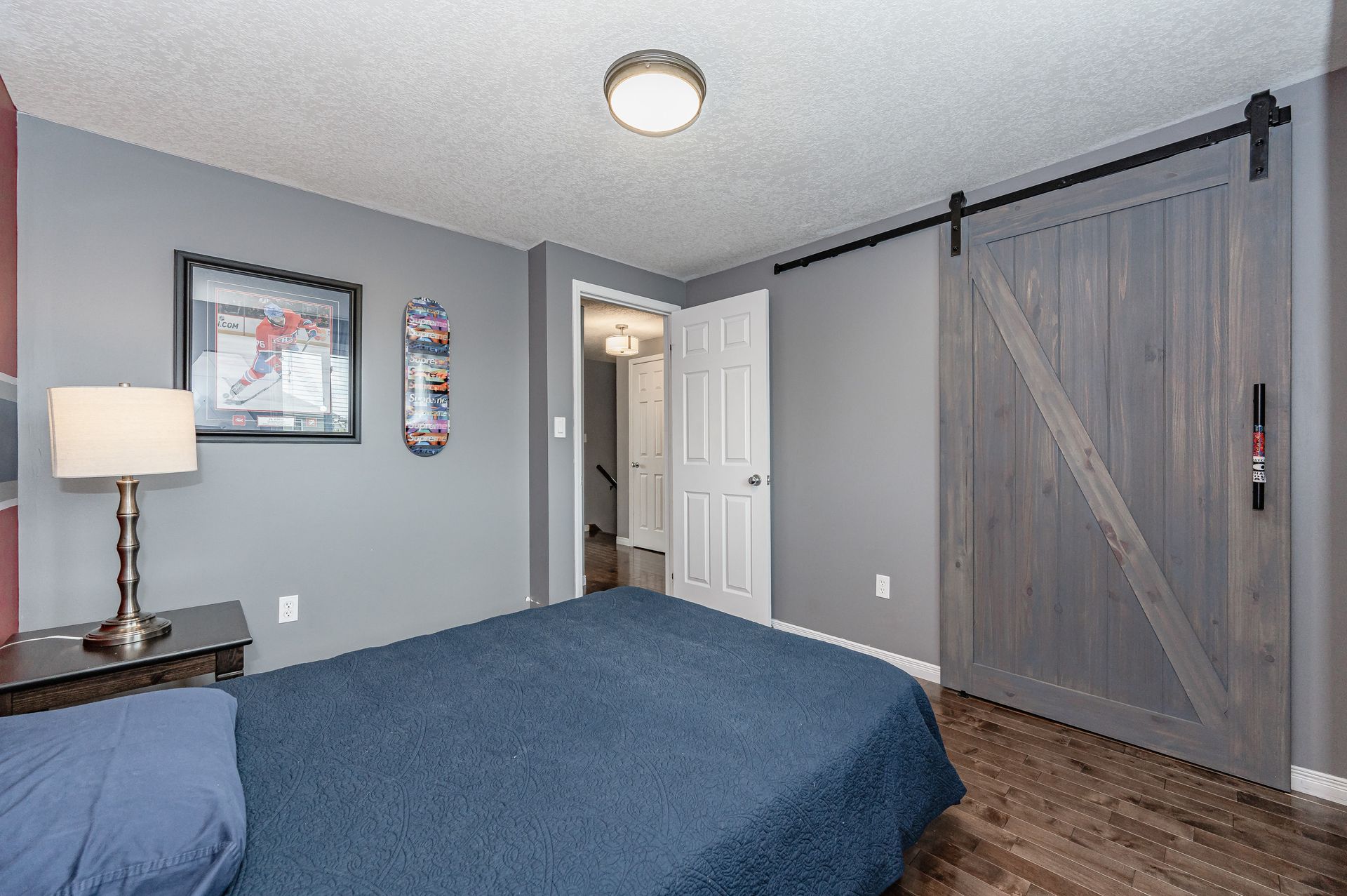 Bedroom with blue bedding, gray walls, framed art, and a rustic sliding barn door.