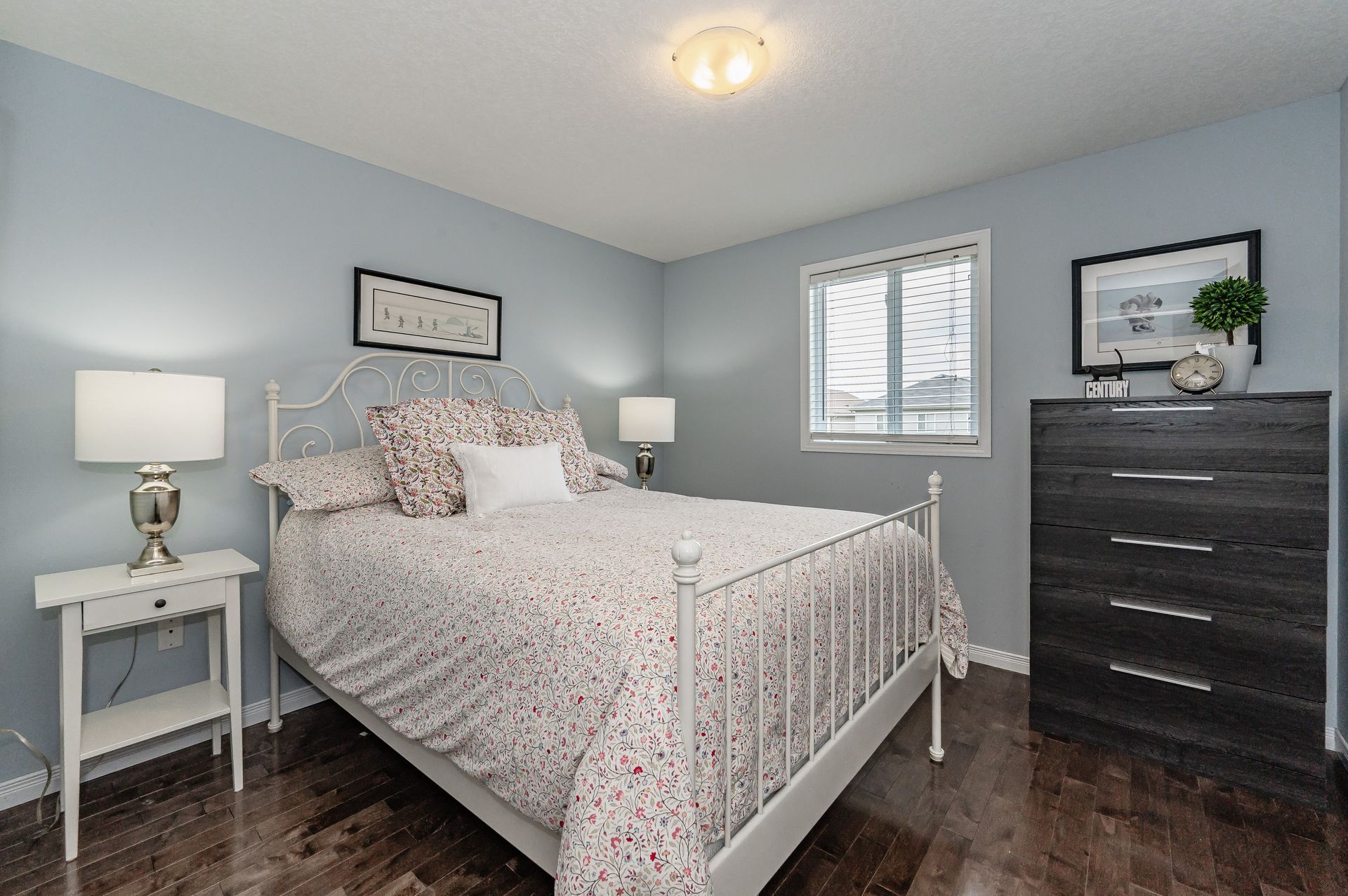 Bright gray bedroom with a white bed, bedside table, dresser, and window blinds