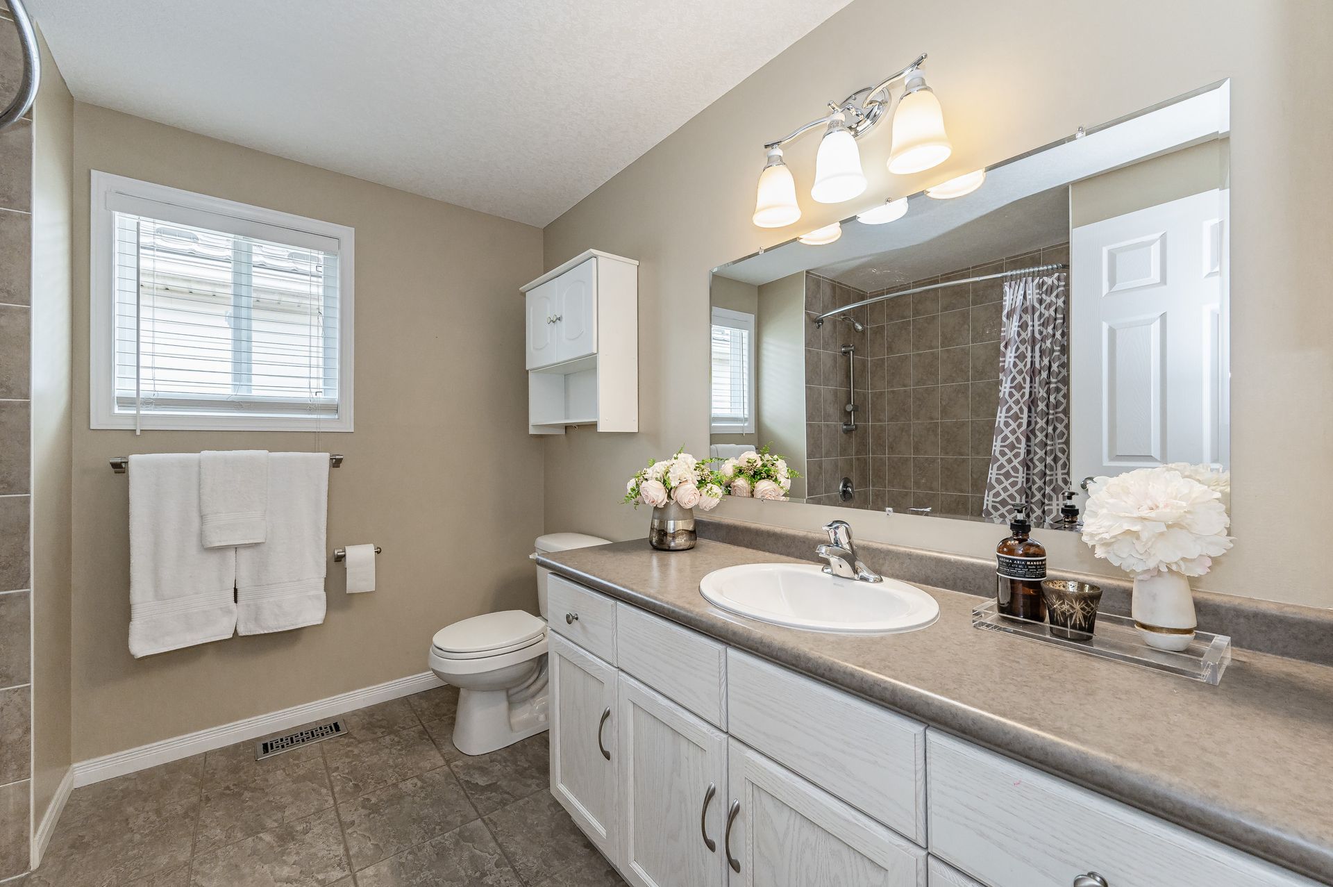 Bright bathroom with double vanity, large mirror, toilet, shower curtain, and beige walls