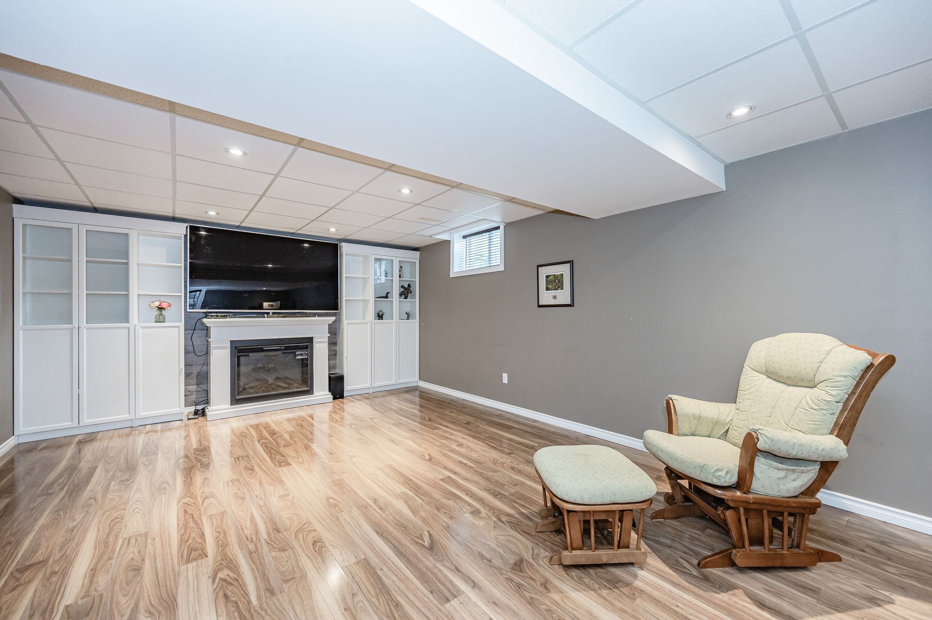 Finished basement family room with fireplace, wood floor, and beige chair and ottoman