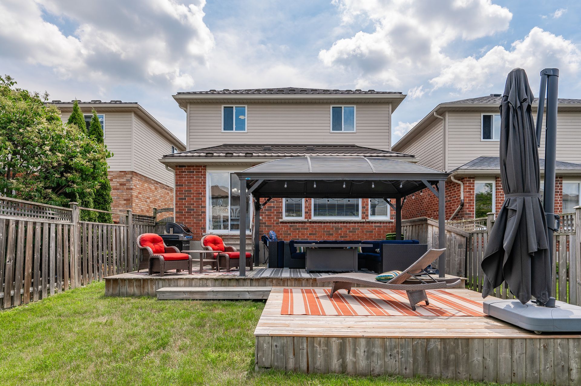 Backyard patio with grill, red chairs, deck, and closed umbrella under a cloudy sky