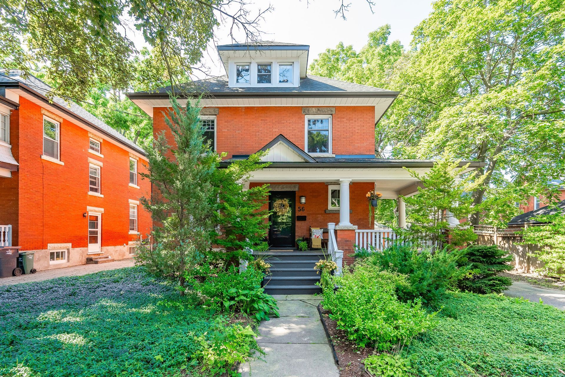 Two-story red brick house with a front porch, steps, and leafy green yard