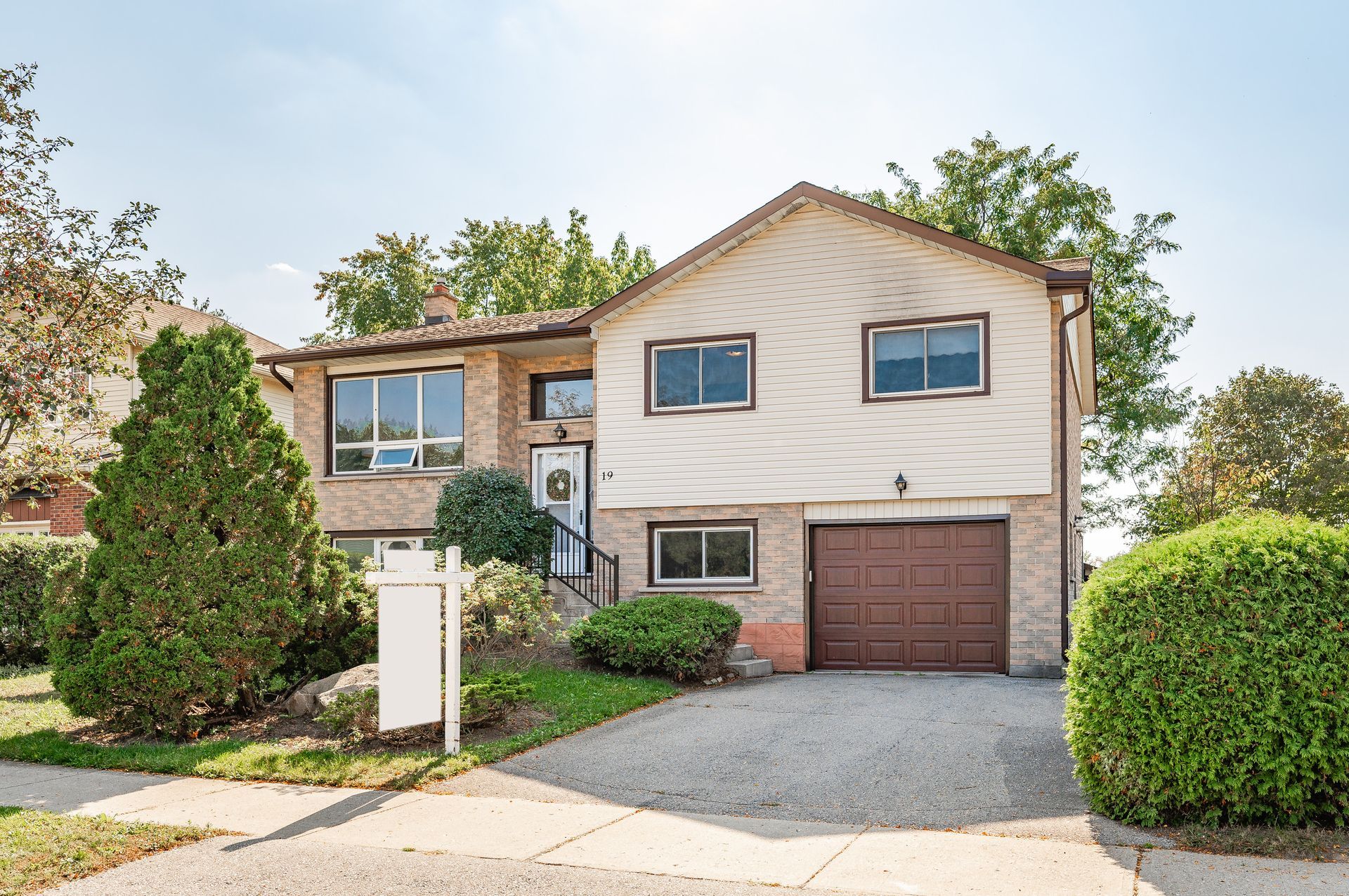Suburban split-level house with beige siding, garage, gravel driveway, and landscaped front yard