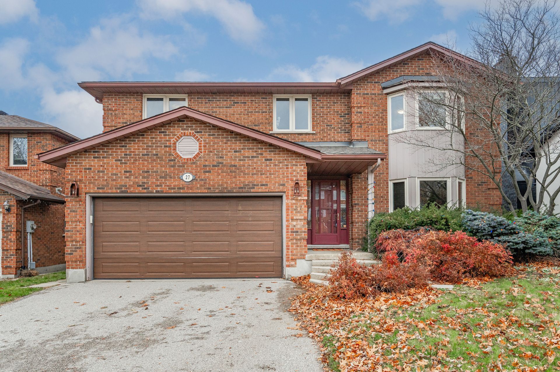 Two-story brick suburban house with brown garage door, driveway, and autumn landscaping