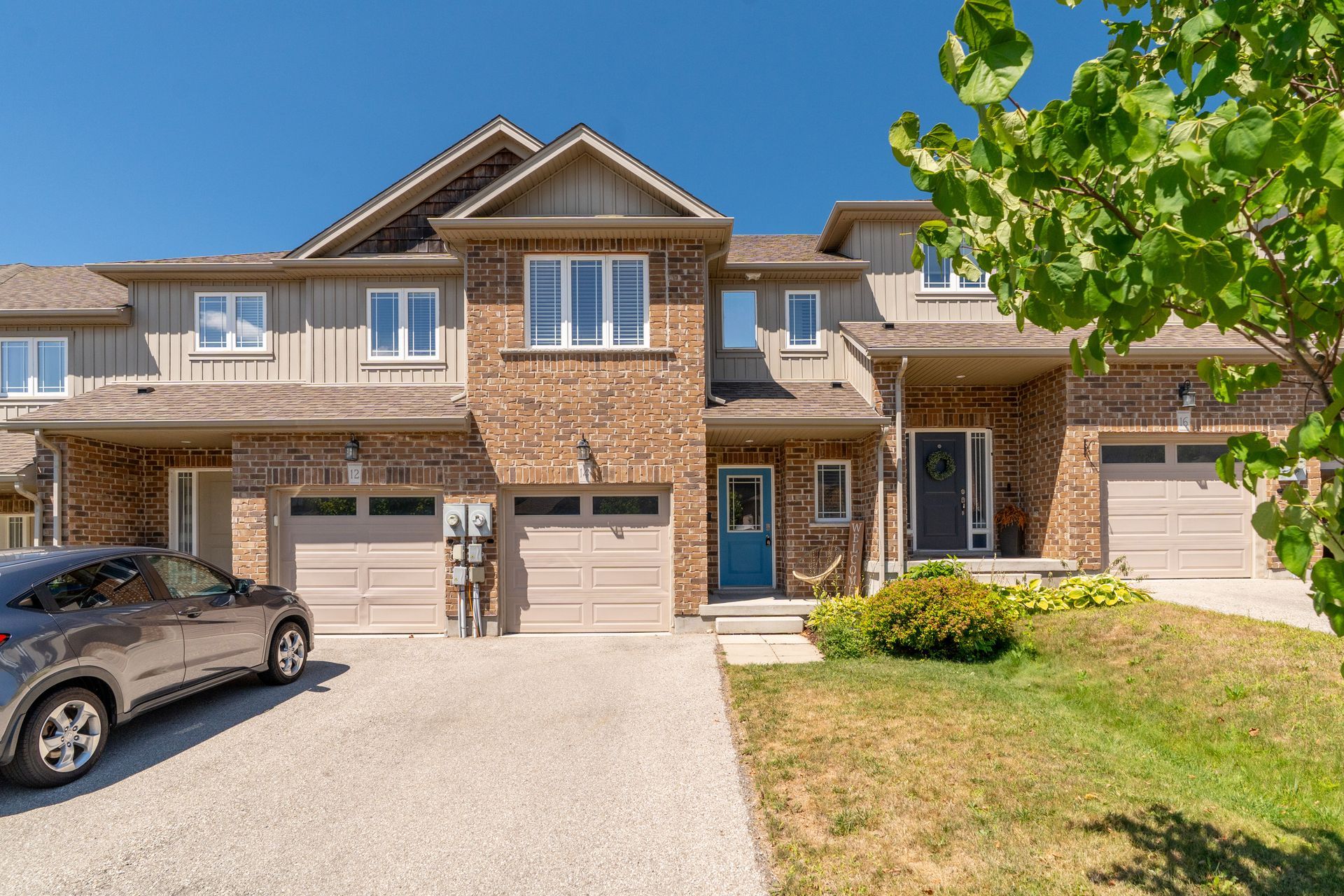 Suburban townhouse with brick facade, two-car garage, and a parked SUV in front under a clear blue sky