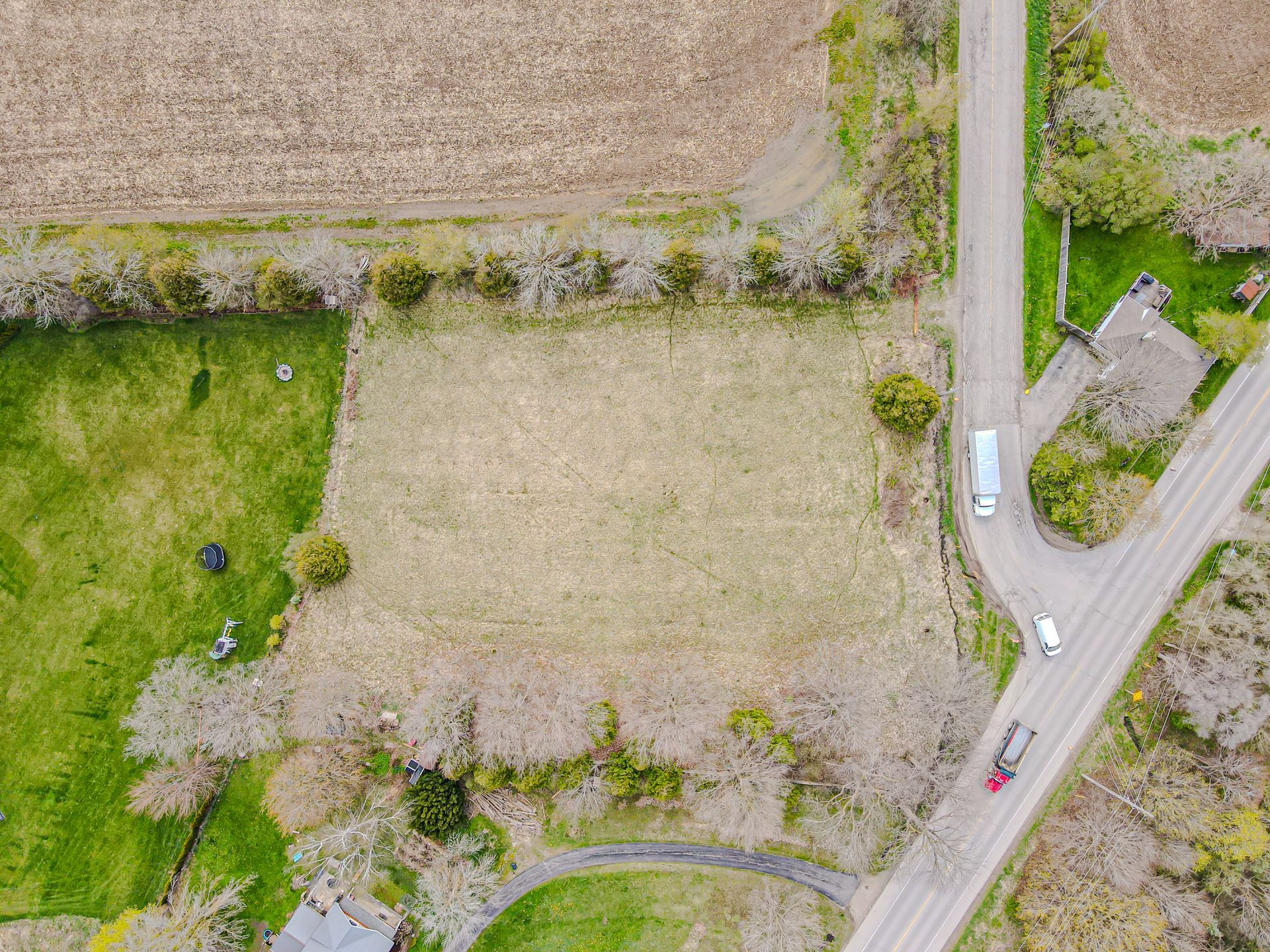 Aerial view of rural fields beside a road intersection with a few cars and trees