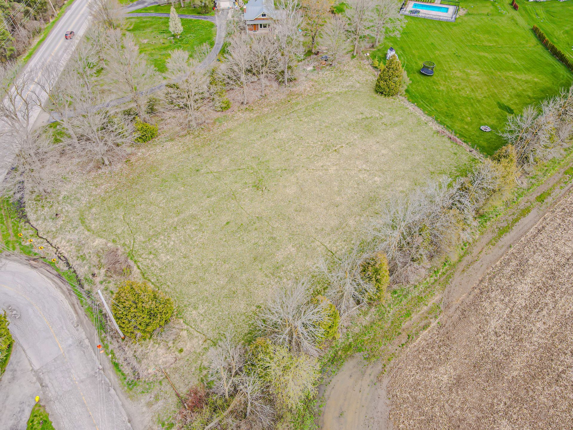 Aerial view of a grassy field bordered by trees, roads, and a small blue structure.