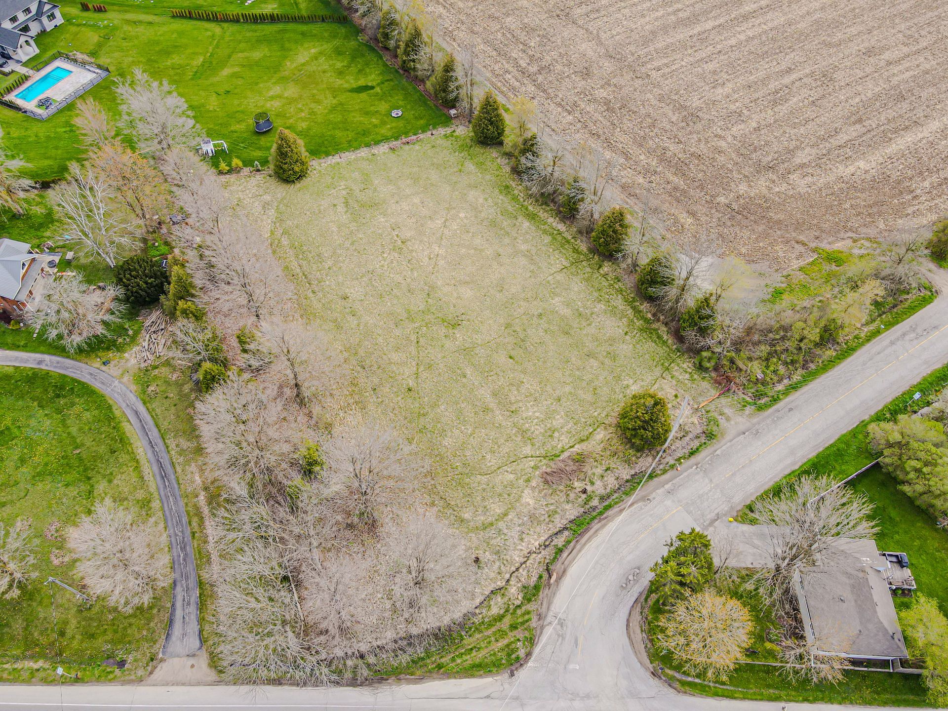 Aerial view of a rural field with roads, trees, and a small house beside a curved lane