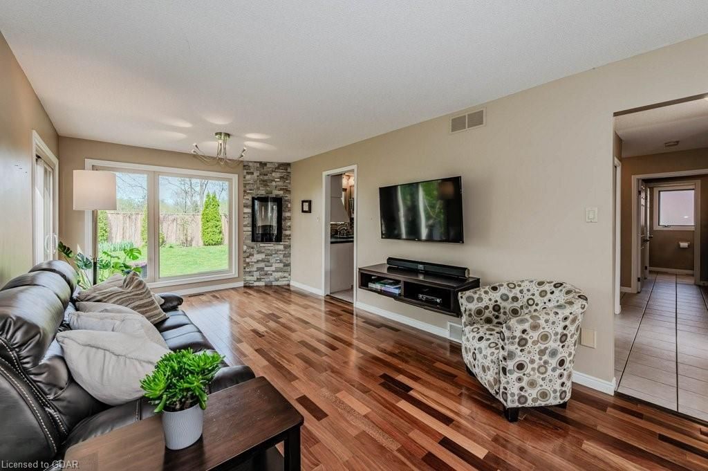 Bright living room with hardwood floors, black sofa, wall TV, and large sliding glass doors overlooking greenery