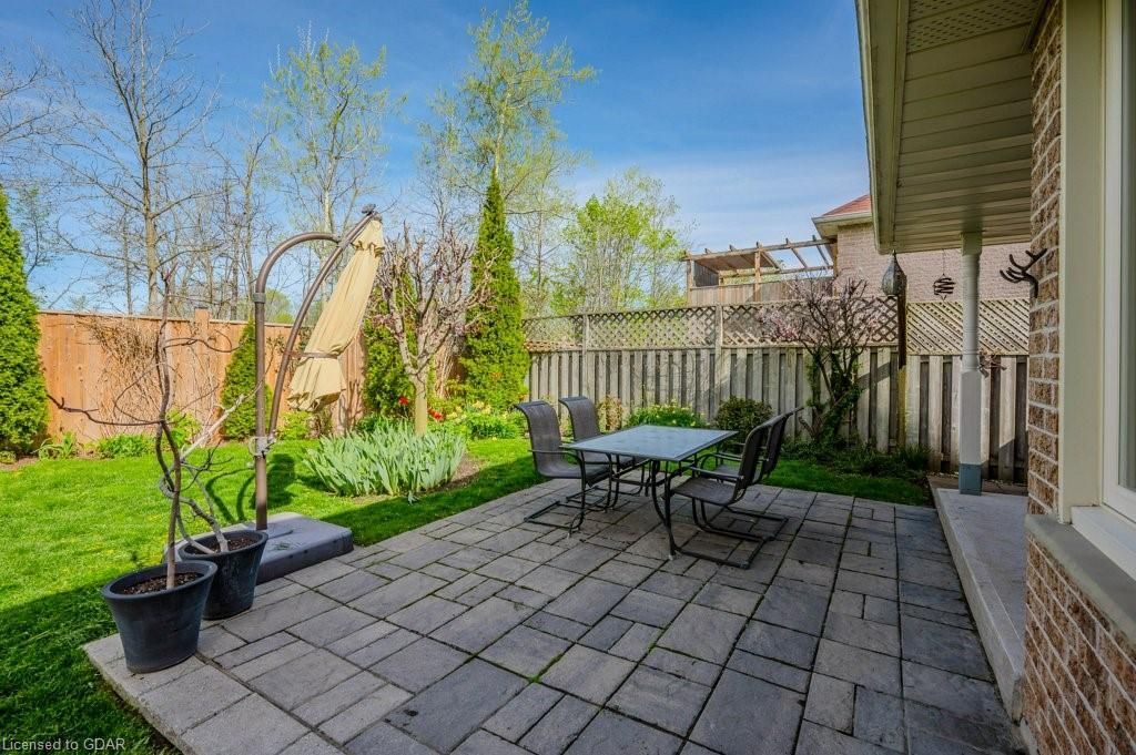 Back patio with patio table, chairs, potted plants, and a grassy backyard fenced by wood and lattice fences