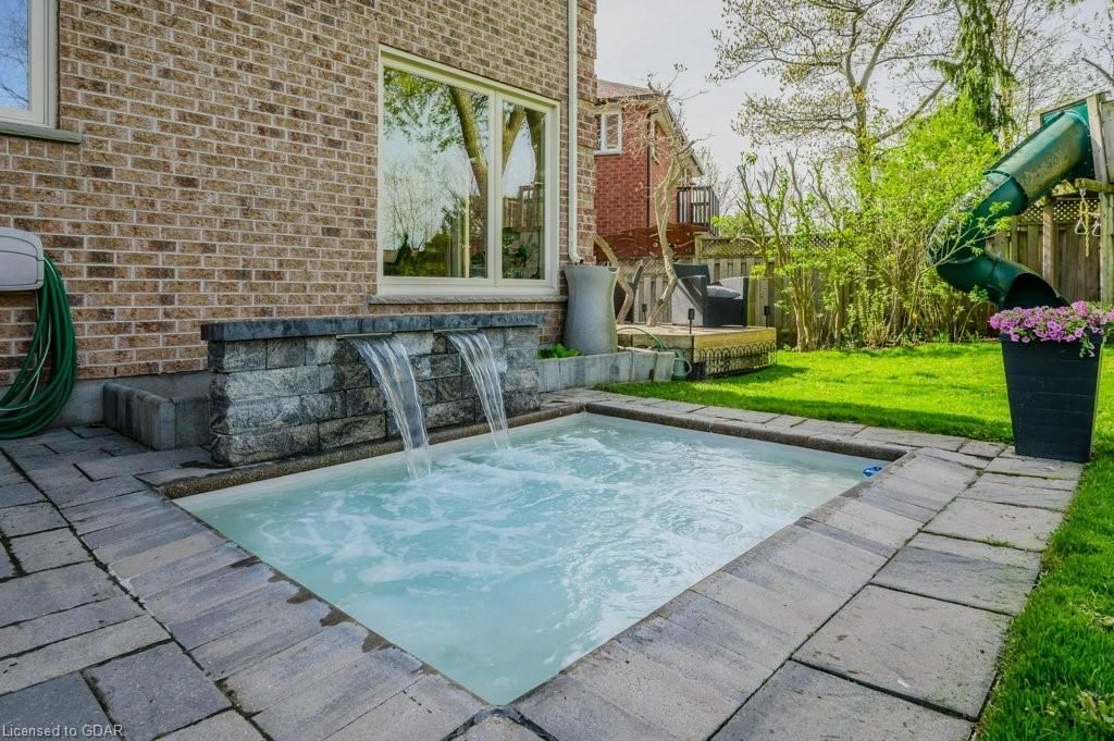 Backyard pool with two water fountains beside a brick house and patio stones