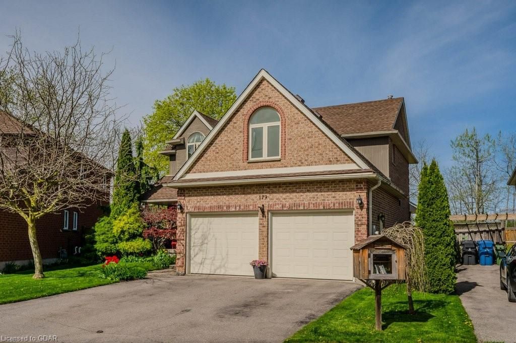 Suburban two-story brick house with double garage, driveway, and landscaped front yard on a sunny day