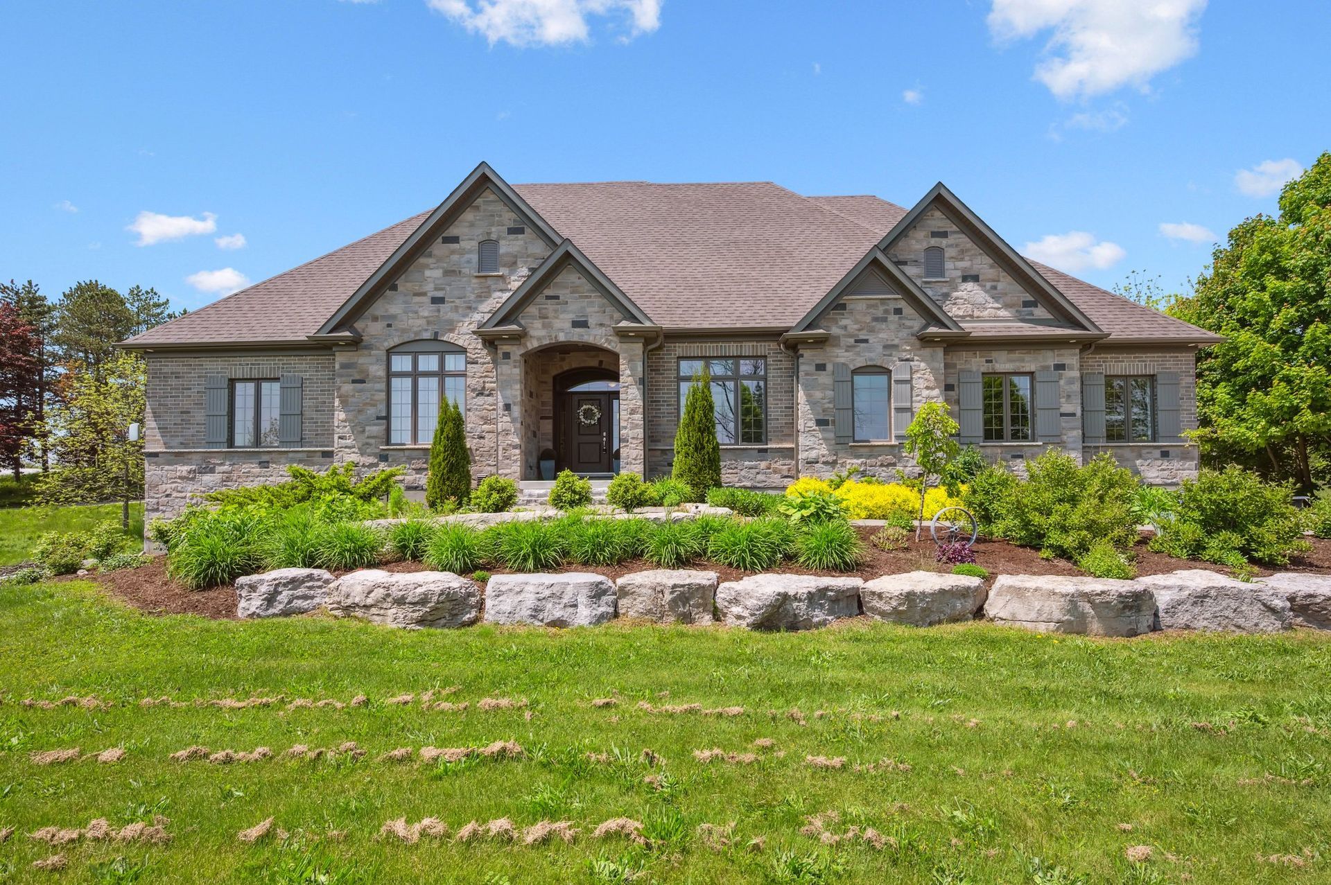 Large stone suburban house with a landscaped front yard and bright blue sky