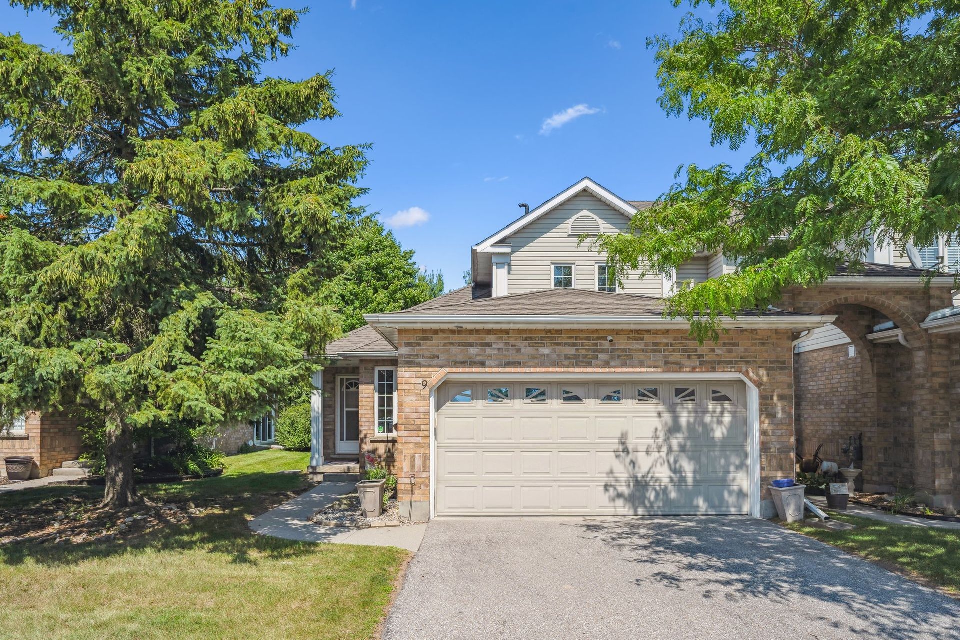 Suburban house with beige garage, stone facade, and green trees on a sunny day