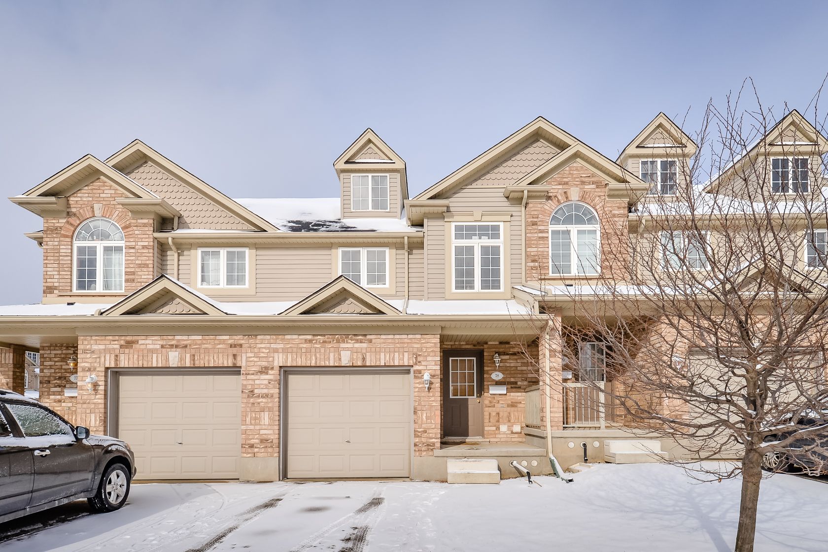 Snow-covered beige townhouse with attached garage and parked car in front