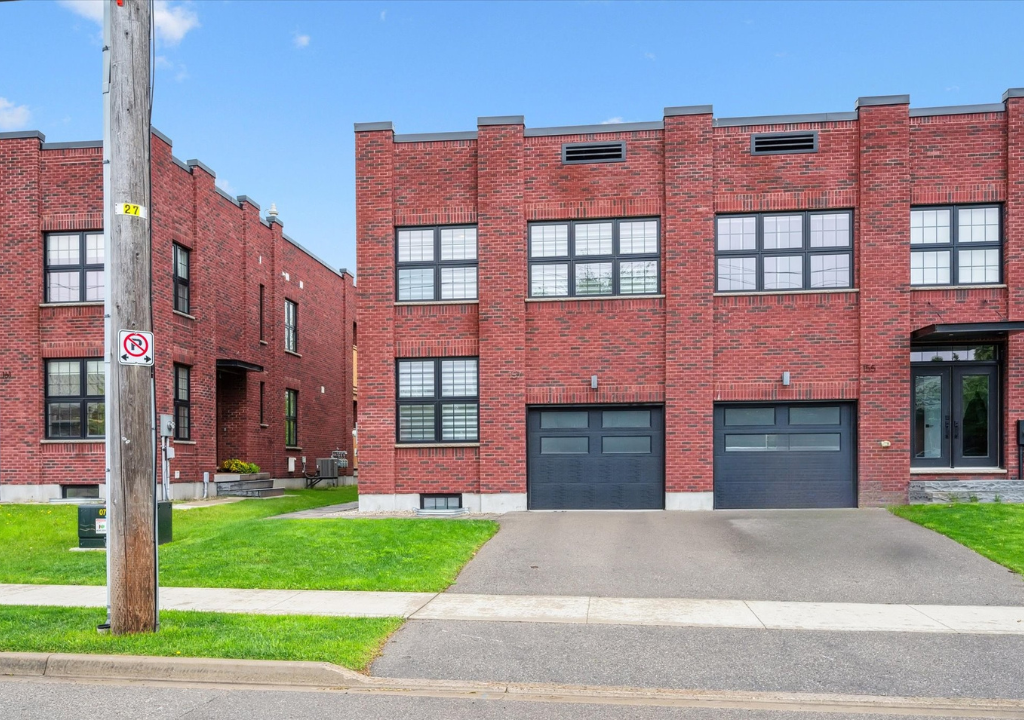 Red brick apartment building with garage doors and a utility pole along a street.