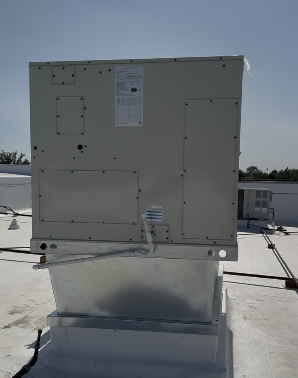 Large beige rooftop HVAC unit on a white roof under a clear blue sky.