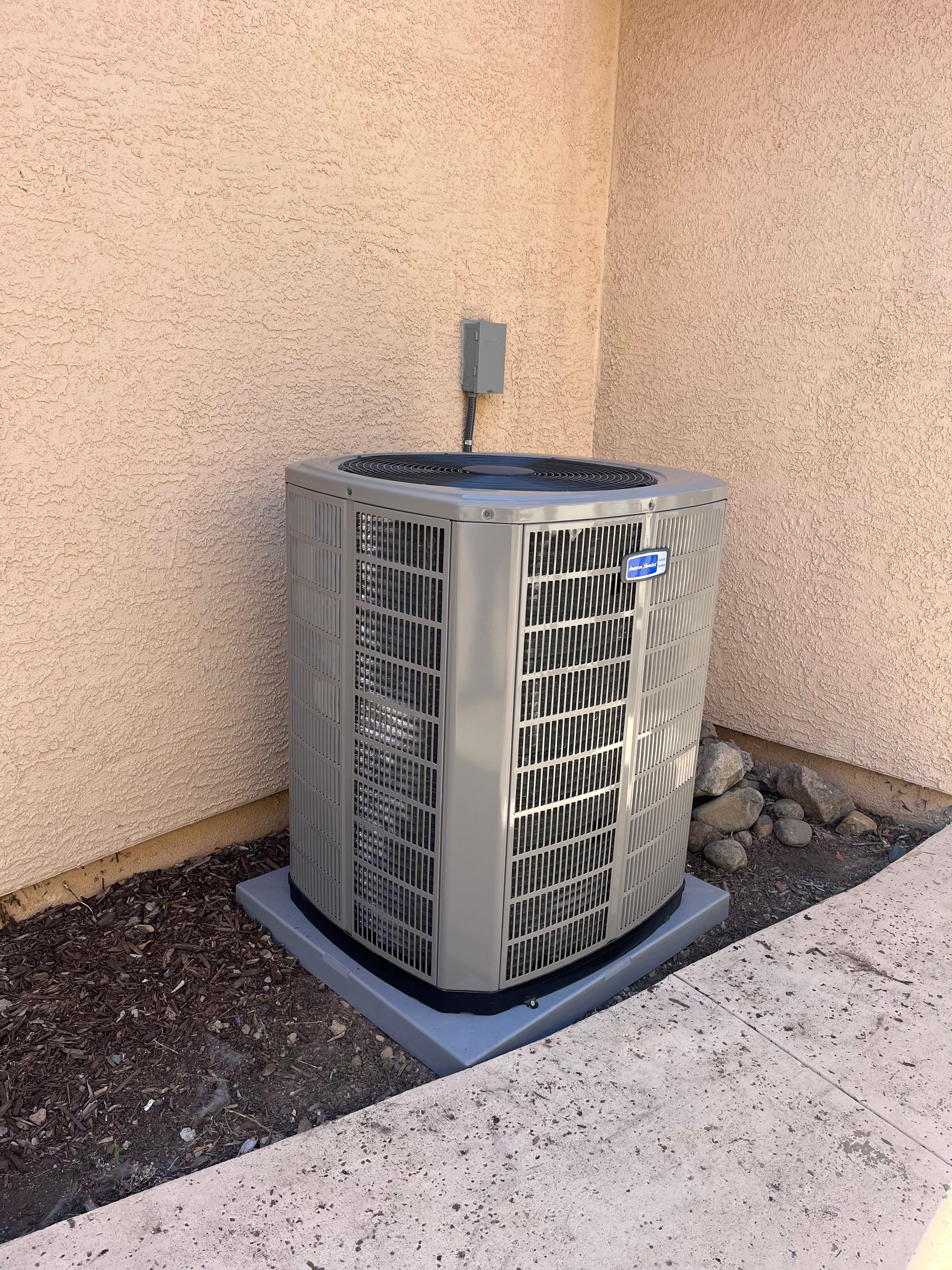 Outdoor air conditioning unit beside a stucco wall on a gravel pad