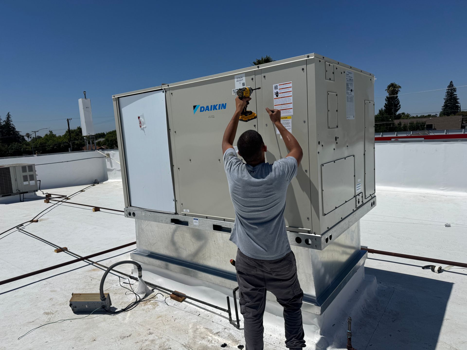 Worker adjusting a rooftop HVAC unit on a flat white roof under a clear blue sky