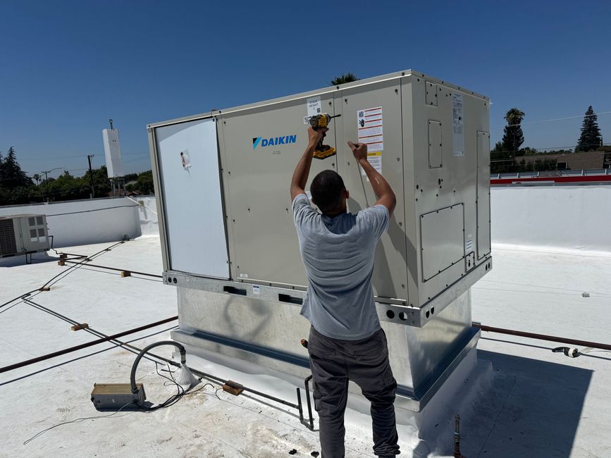 Worker adjusting a rooftop HVAC unit on a flat white roof under a clear blue sky