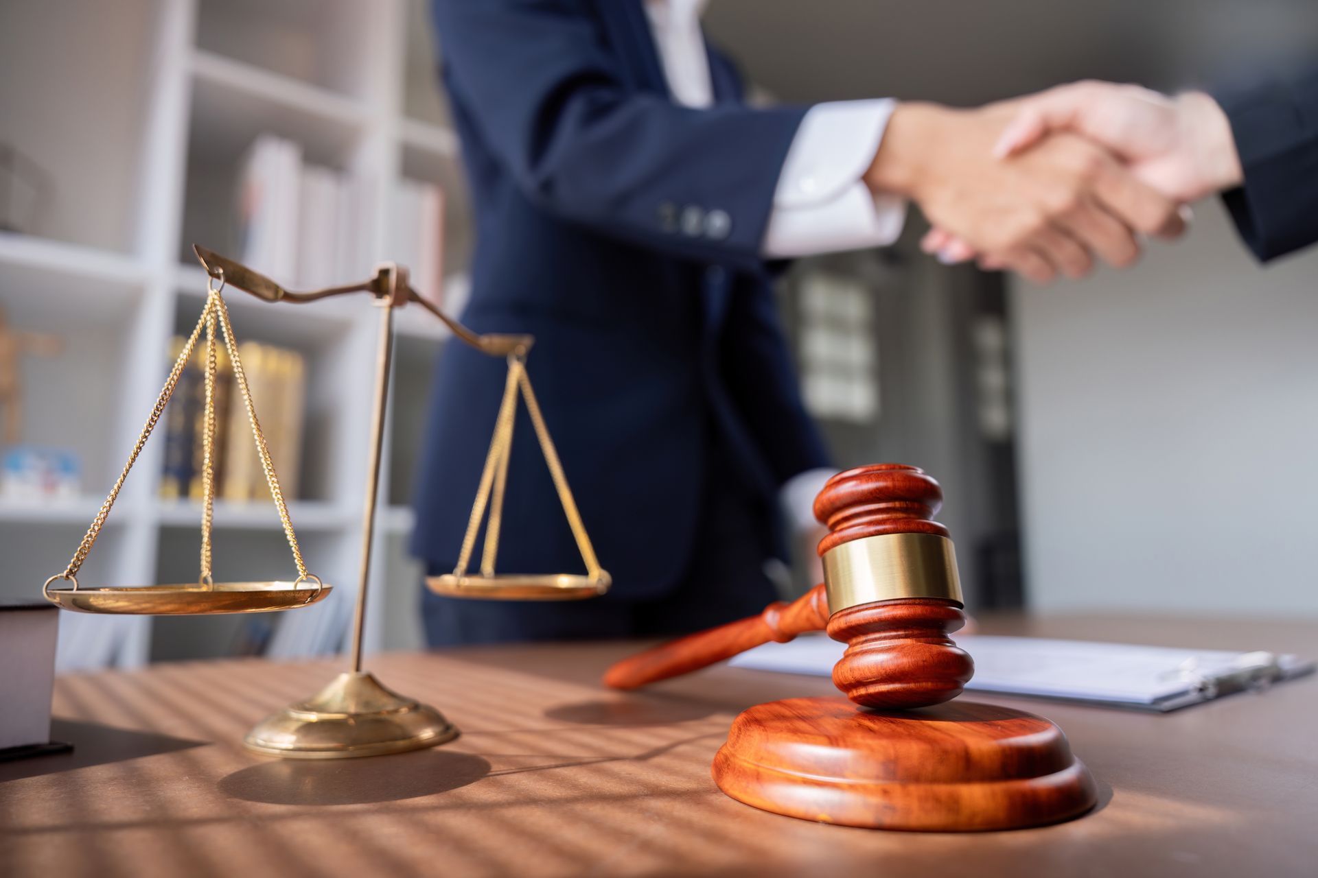 A judge shaking hands with a client in front of a scale of justice.
