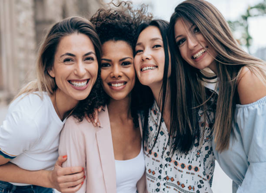 Four smiling women, embracing outdoors.